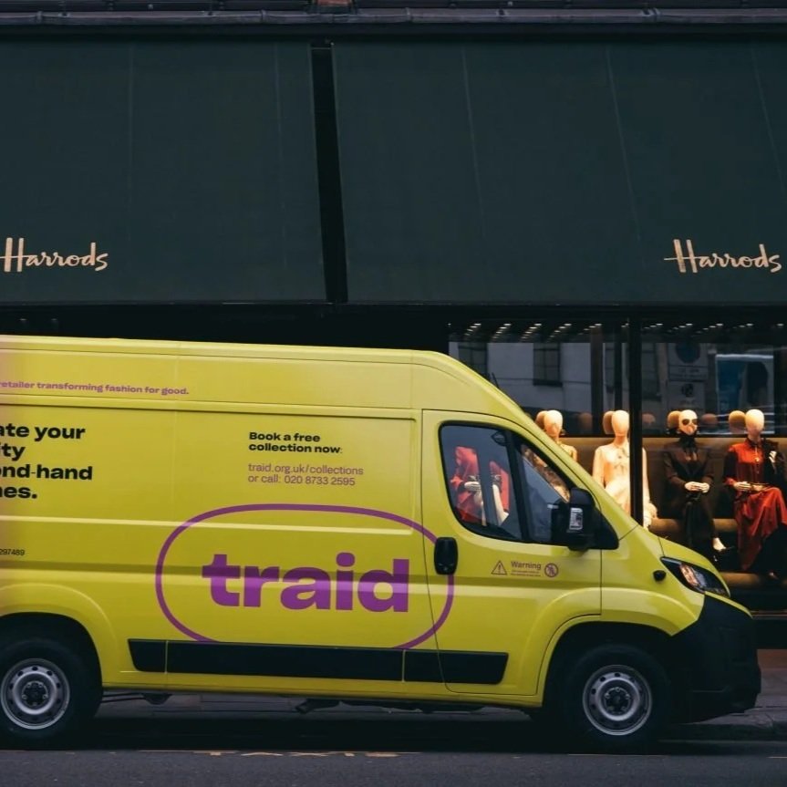 A yellow van with 'traid' on the side in purple, driving past Harrods.