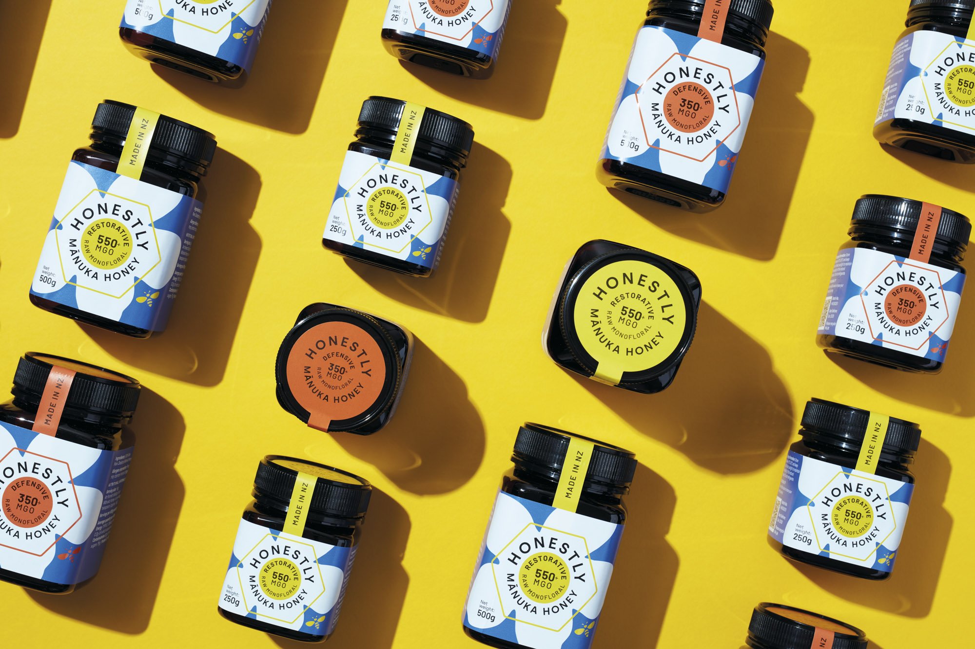 Four jars of Honestly Manuka Honey in different strengths and sizes displayed against a bright yellow background..