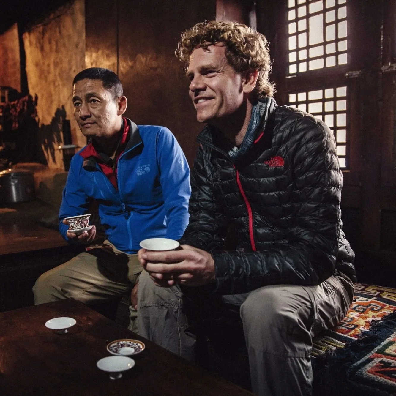 Sherpa Tenzing sitting with TENZING founder Huib van Bockel in a rustic room.