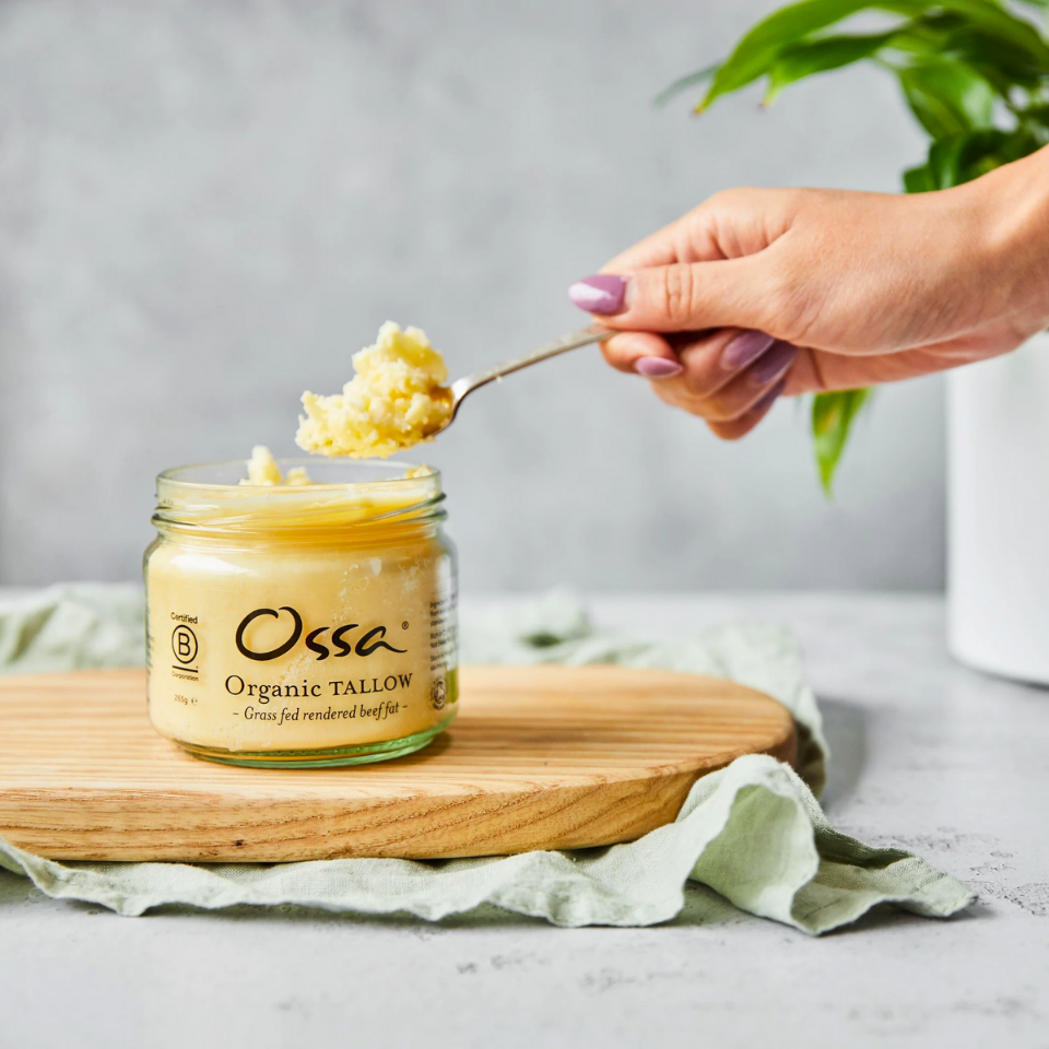 A manicured hand scoops out some Ossa Organic Tallow on an attractive tabletop.