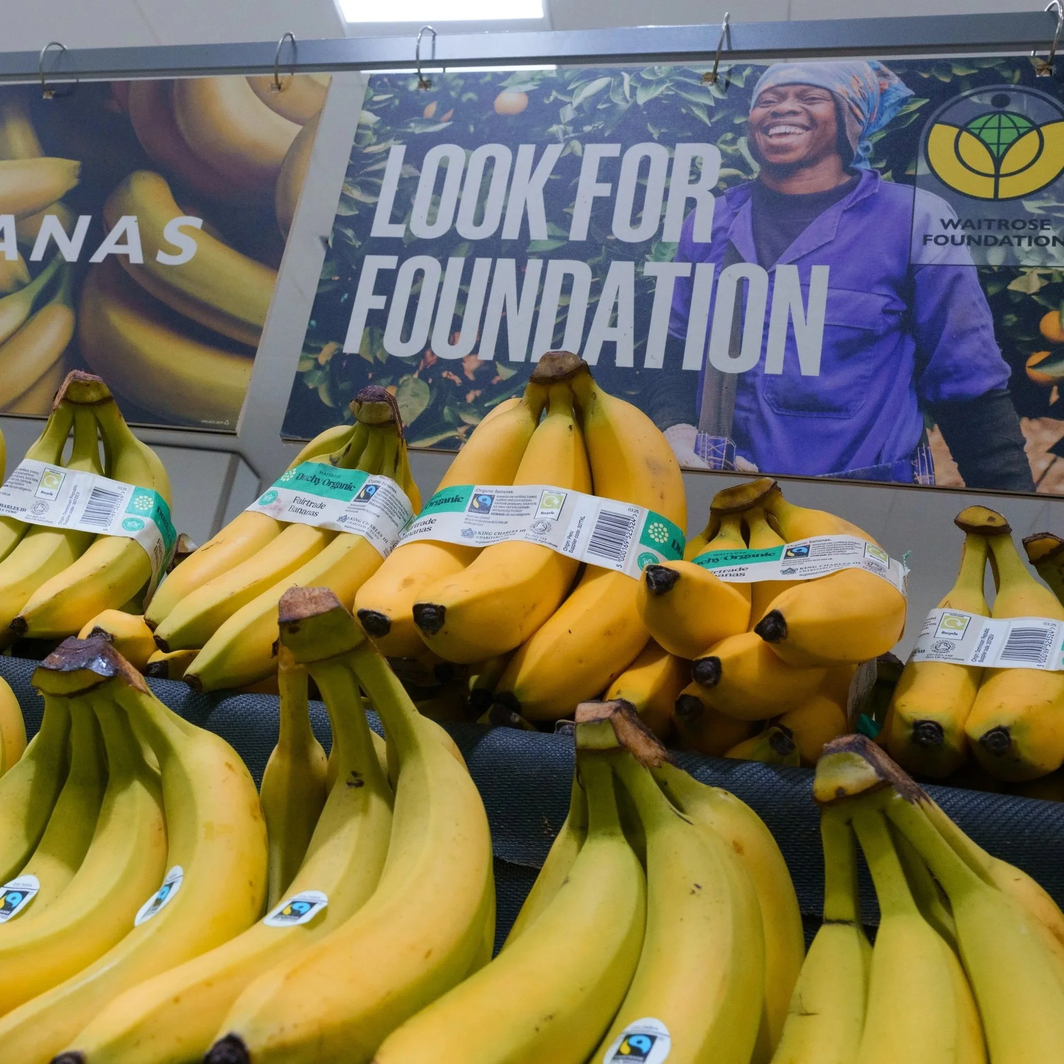 Bunches of Fairtrade bananas stacked in front on Waitrose Foundation signage