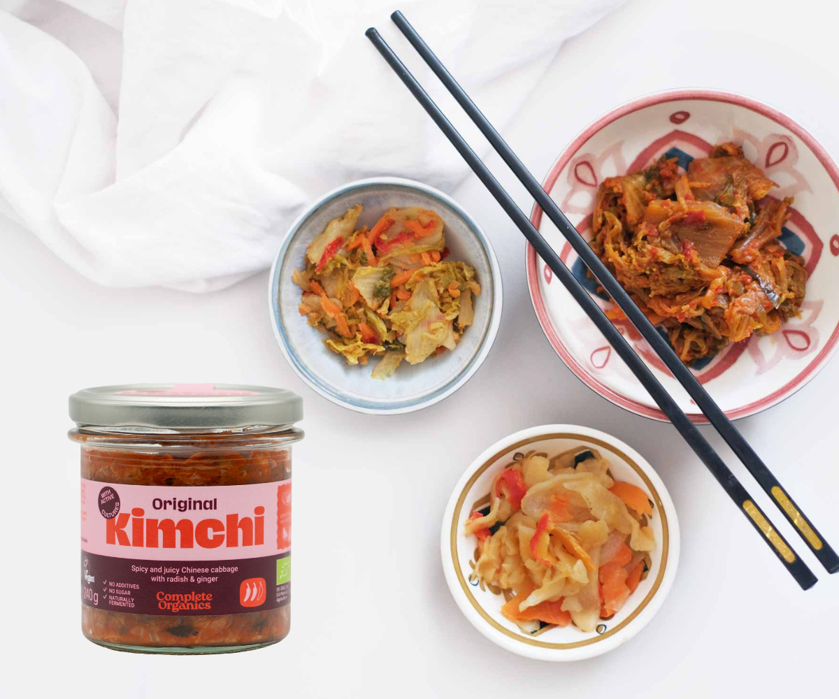 A packshot of Complete Organics Kimchi next to bowls of Asian-inspired food