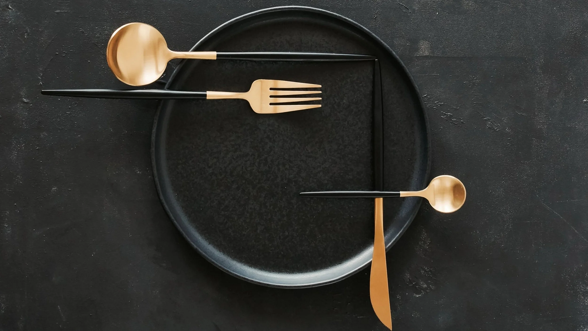 Gold-tipped cutlery artfully presented against a black frying pan.