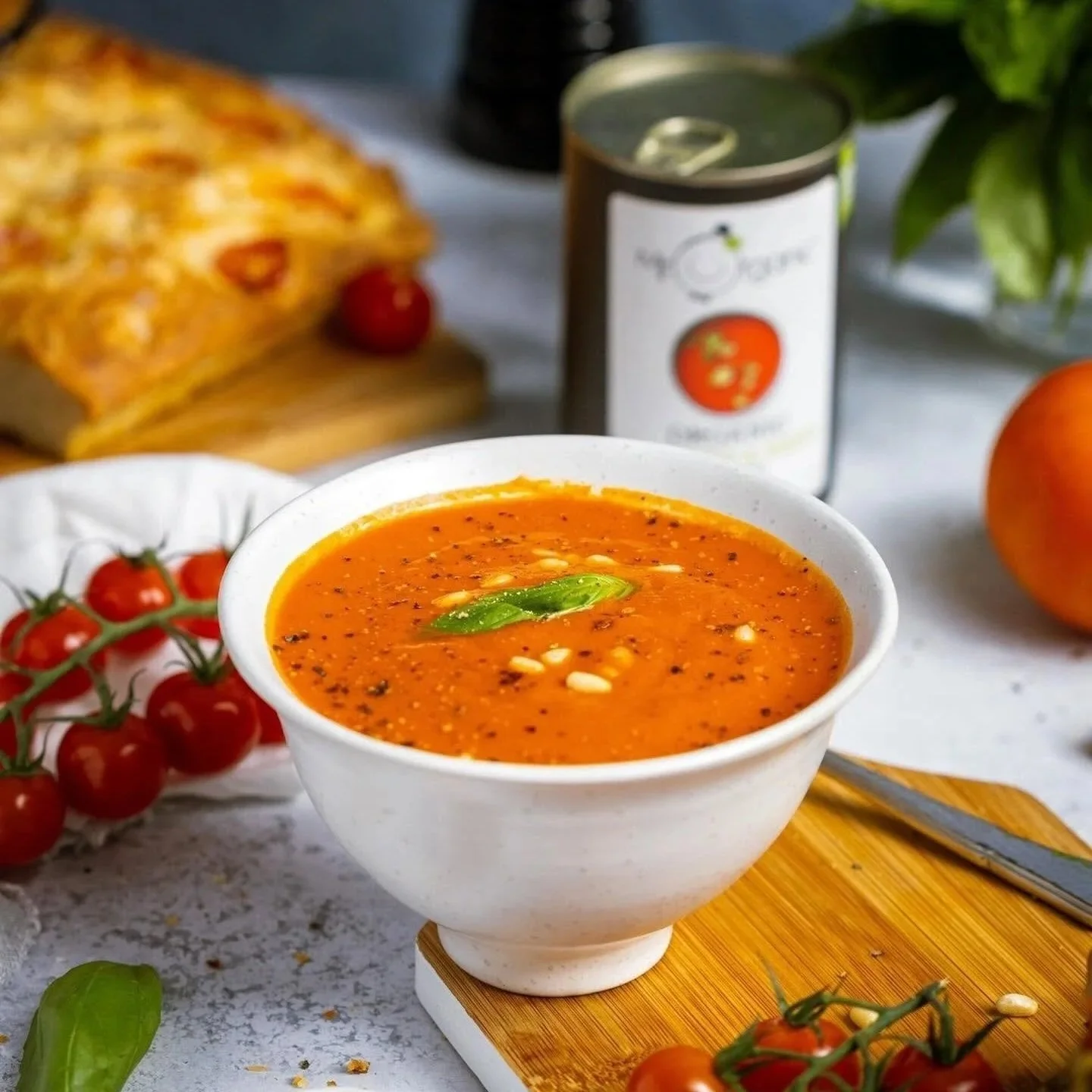 Bowl of Mr Organic bean soup on a wooden board alongside vine tomatoes.