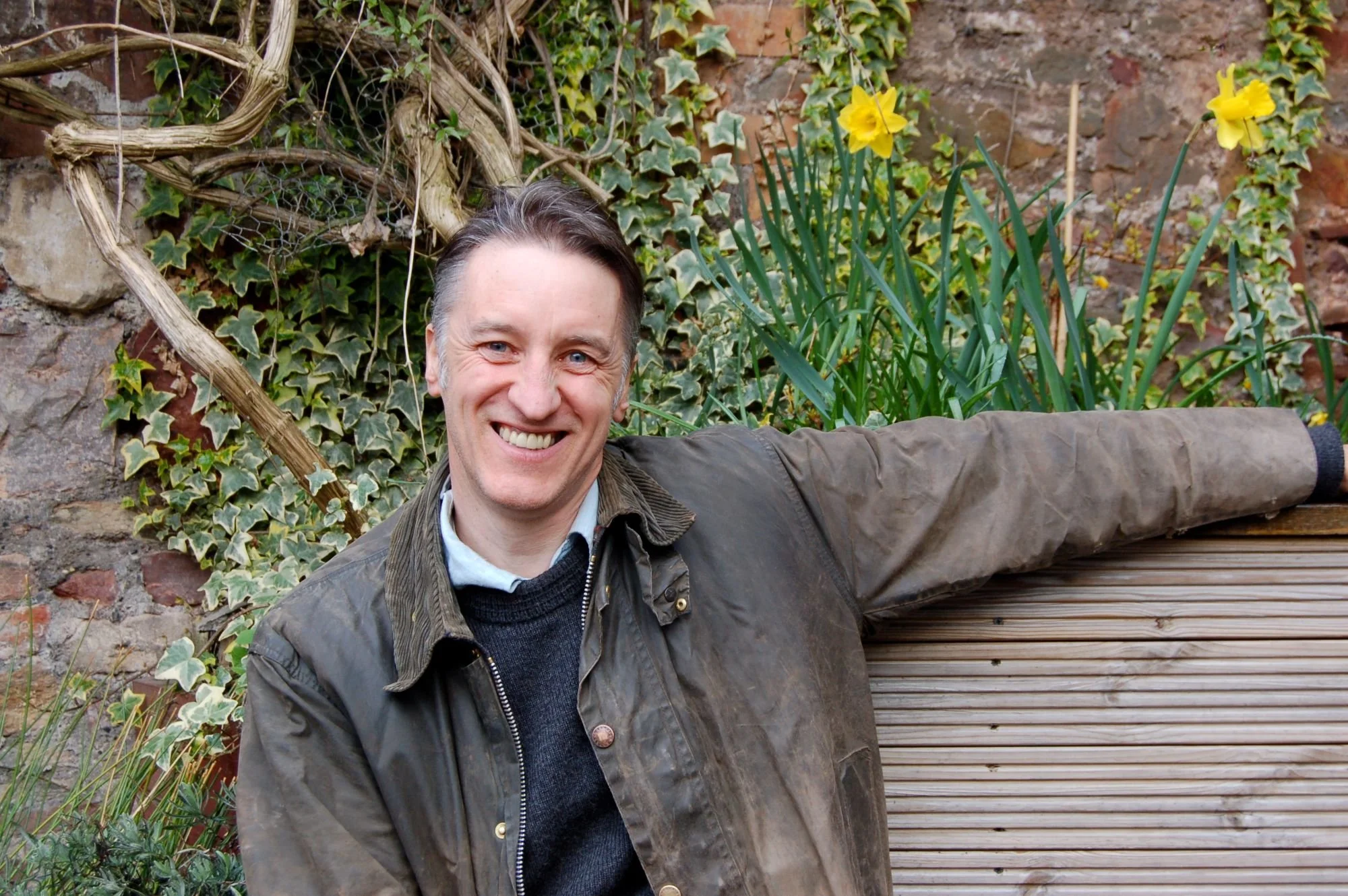 Phil Haugton sitting on a wooden bench in front of a wall of ivy