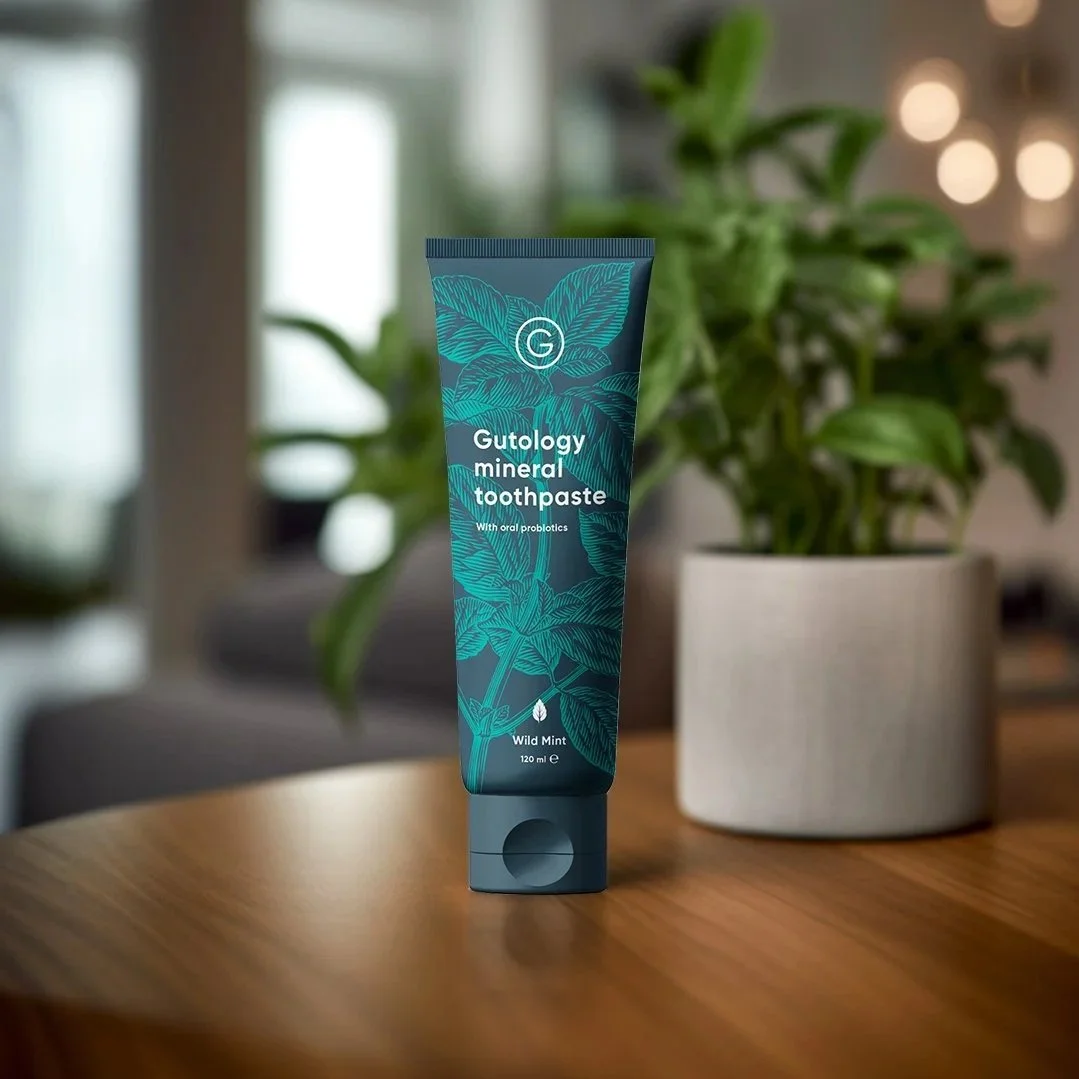 Tube of Gutology toothpaste with green leafy plant in background.