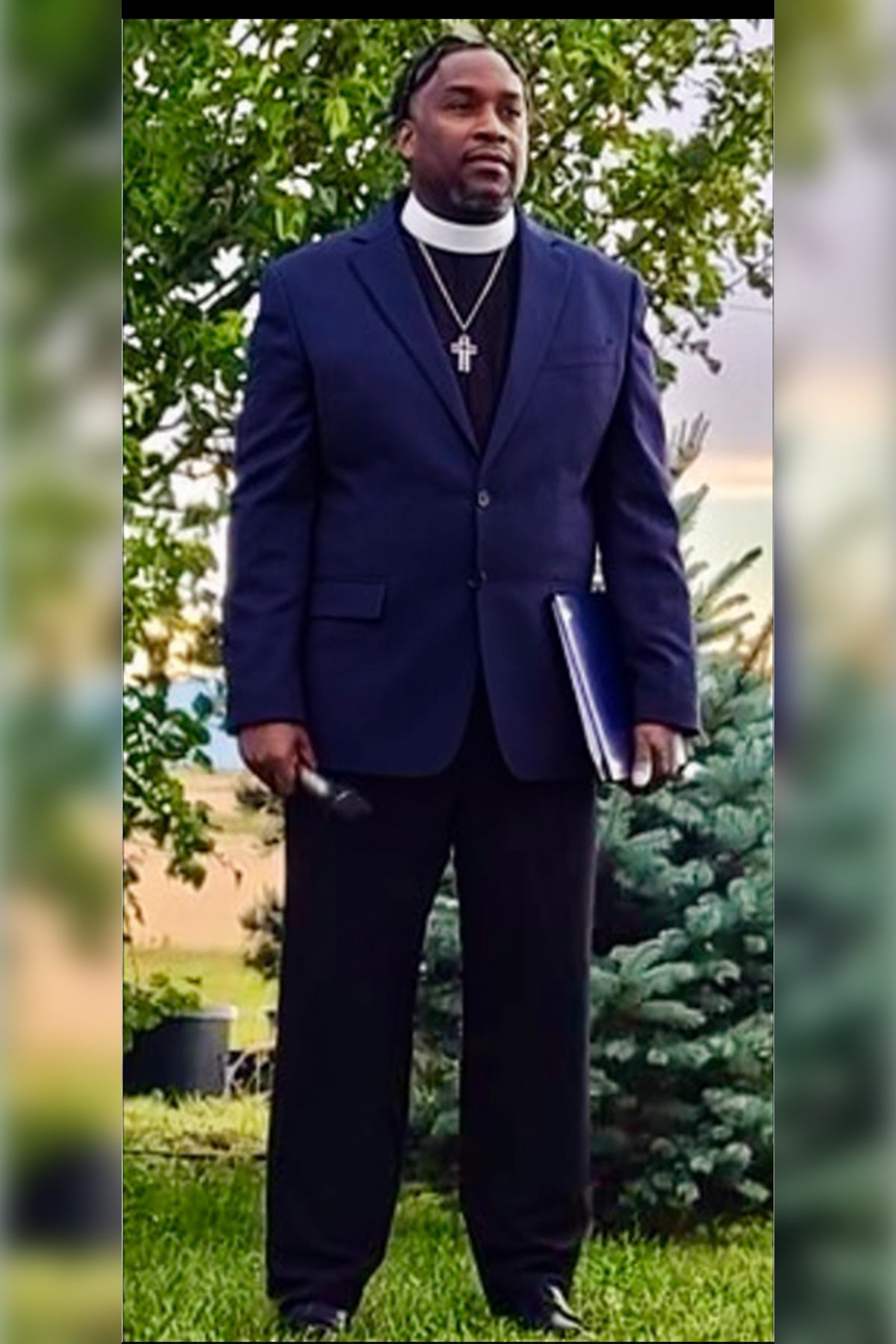 Pastor Terry Newman wearing clerical attire and a cross necklace outdoors.