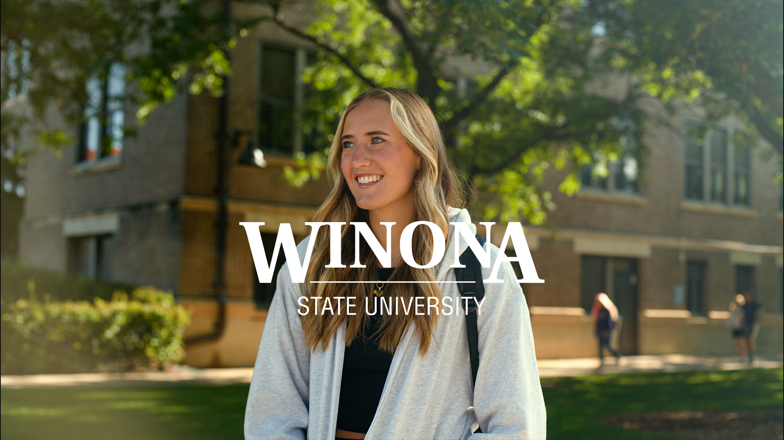 A young woman with long blonde hair and a backpack smiling outdoors on a university campus with trees and brick buildings in the background, overlaid with the text 'Winona State University'.