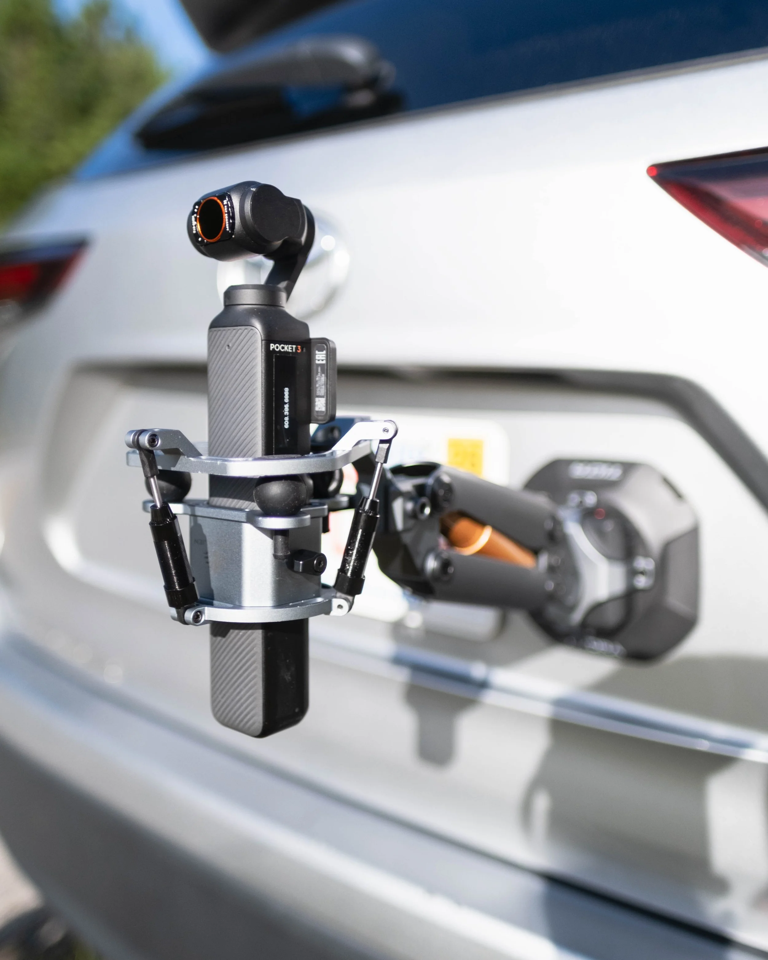 Film crew on outdoor set with camera operator and director during daytime, surrounded by green grass and trees.