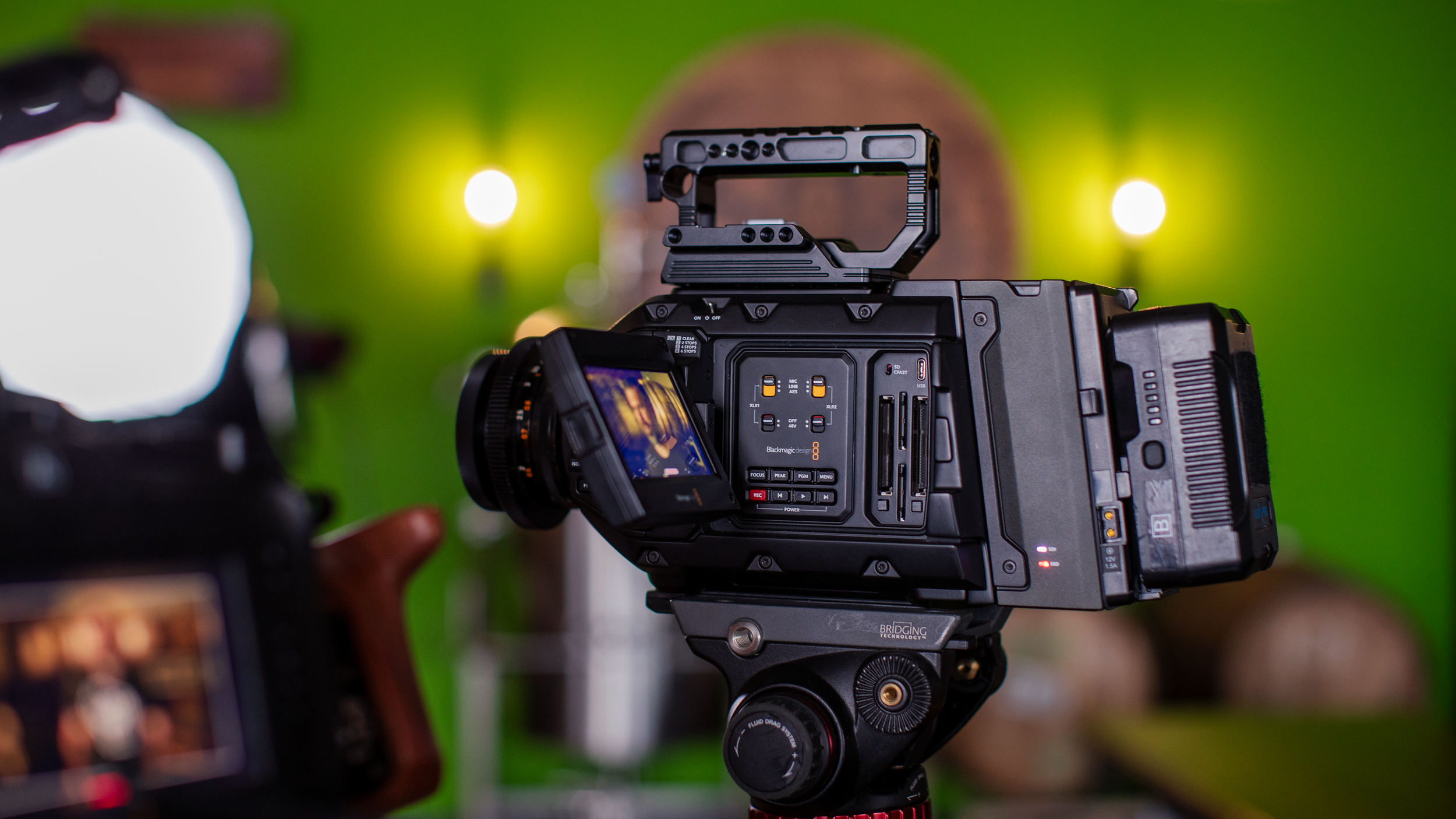 Professional video camera set up on a tripod with a green screen background in a studio.