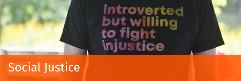 a person wearing a black t-shirt with the text "introverted but willing to fight injustice"