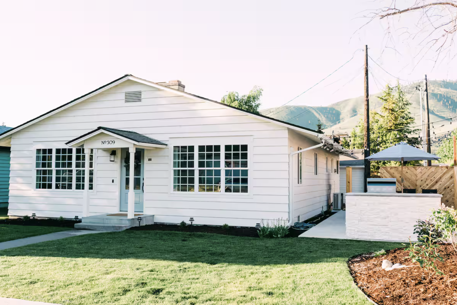 Living room with wood-paneled ceiling, large windows, and a vaulted ceiling with skylight. Includes a dark green sofa, a beige armchair, a round wooden coffee table, a flat-screen TV, and a wood-burning stove.