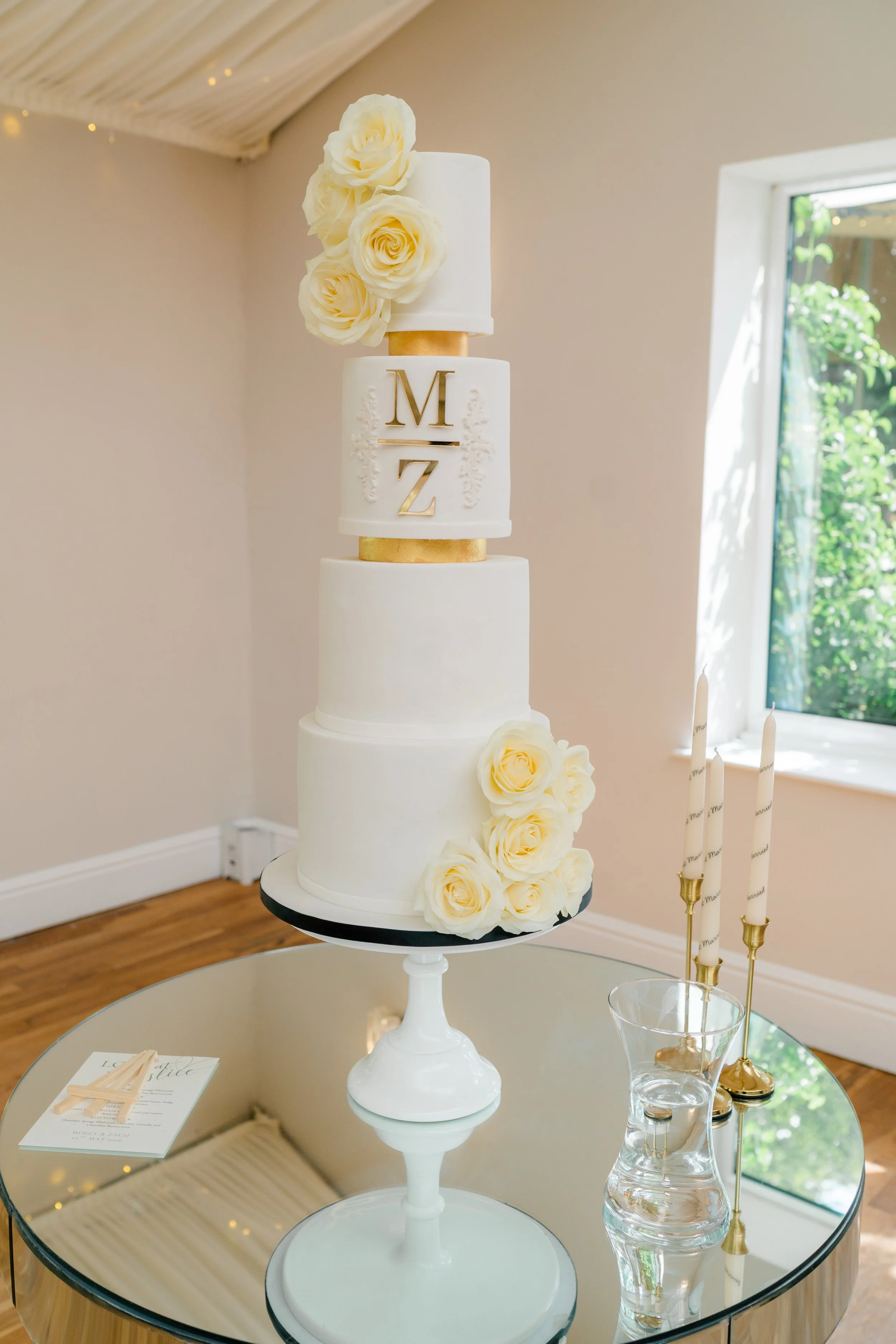 Four-tier white and gold wedding cake with fresh roses at Wrenbury Hall