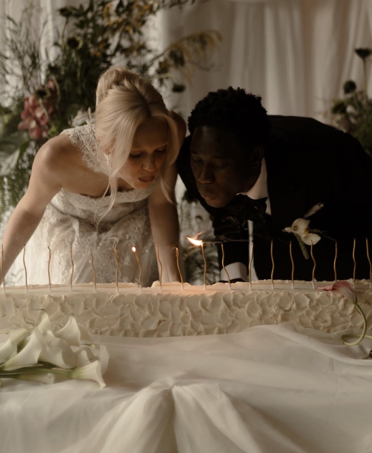 couple blow out candles on a long wedding cake