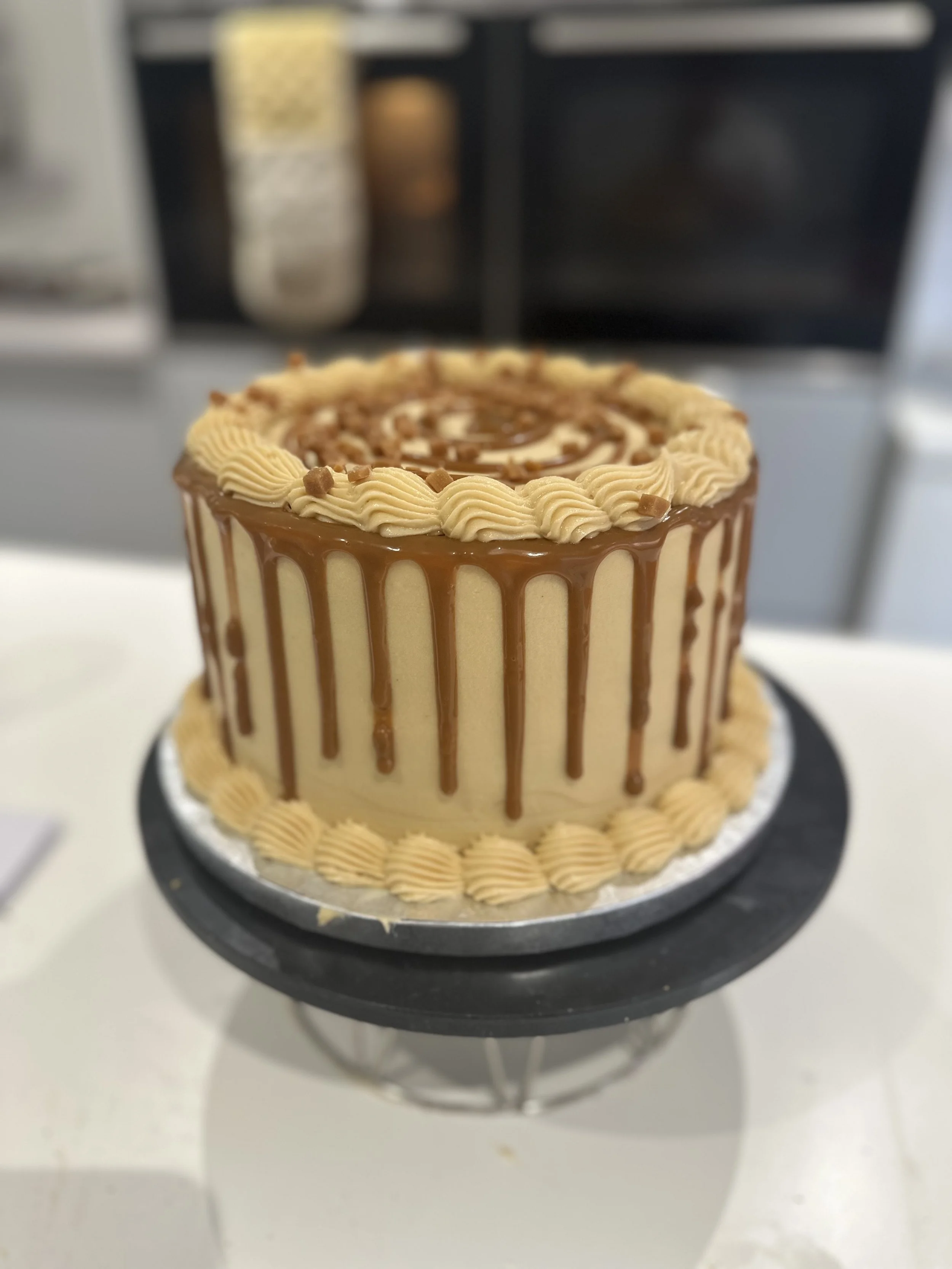 Caramel drip cake with piped. buttercream prepared by Merryfall Cakes Bakery