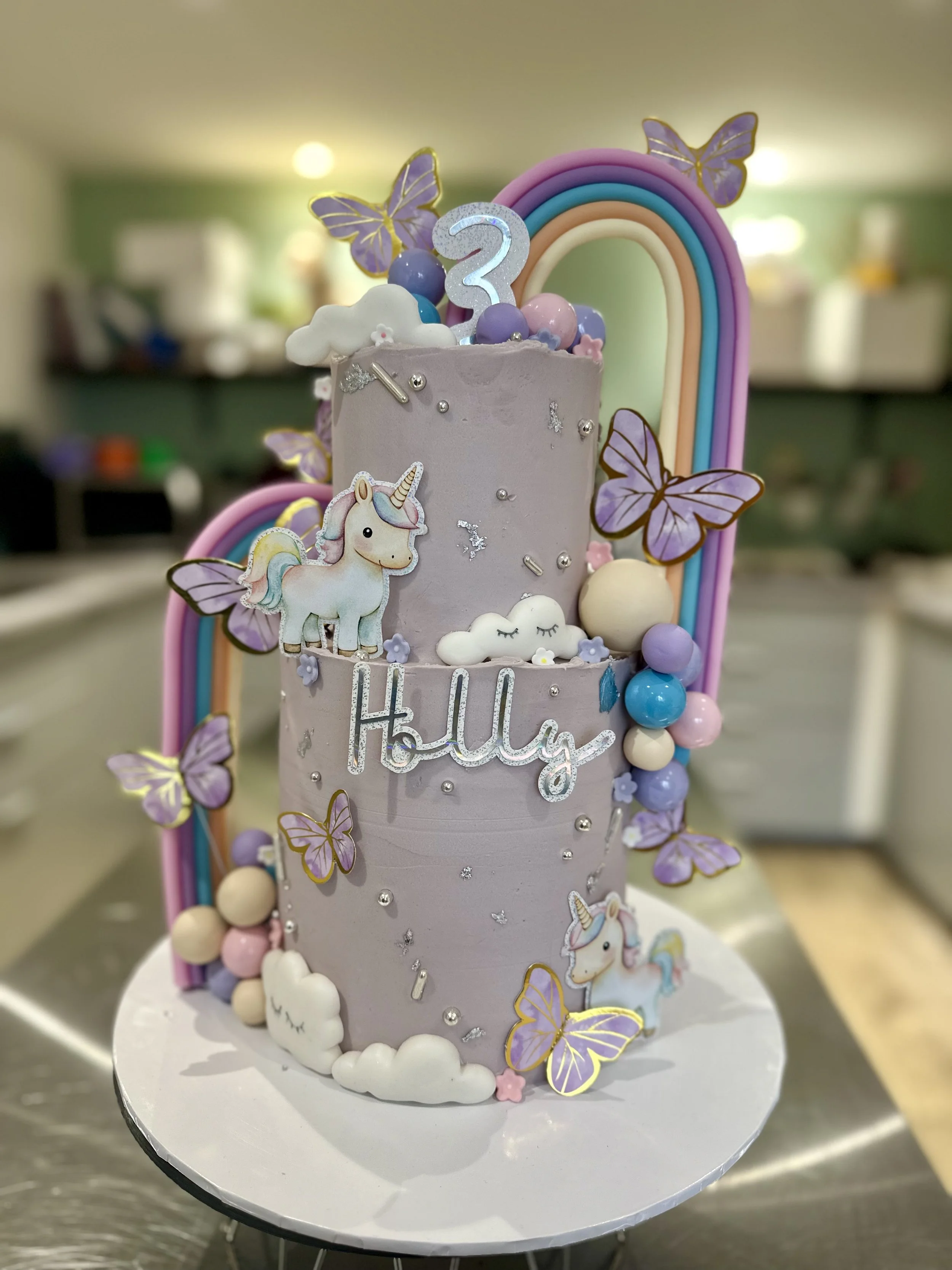 Pastel rainbow birthday cake with butterflies, clouds and personalised name