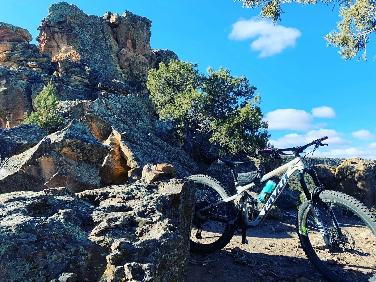 Mountain bike on rocky terrain with large rock formations and trees under a clear blue sky.