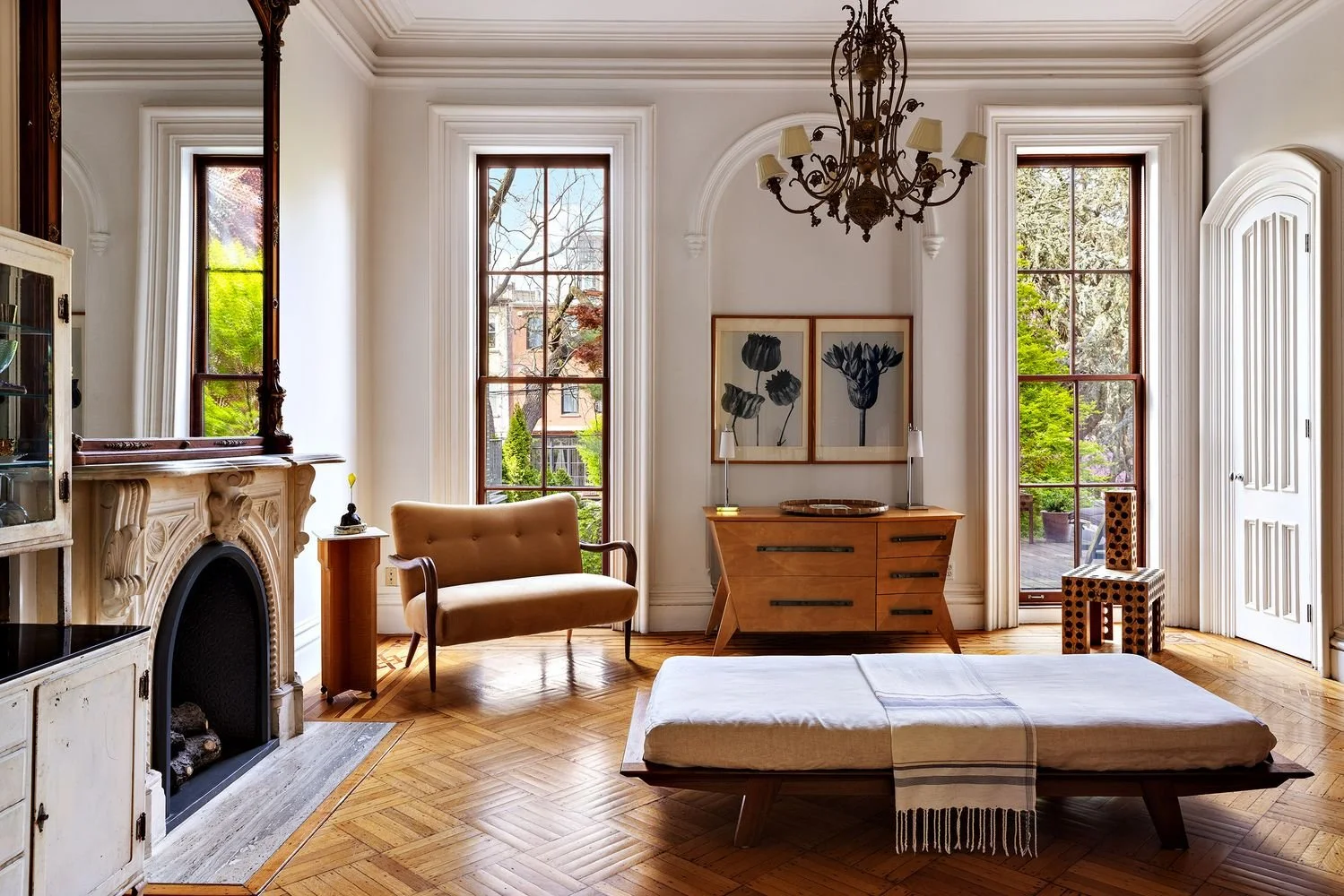 Living room with tall windows, wooden furniture, a fireplace, a chandelier, and a bed with a throw blanket.