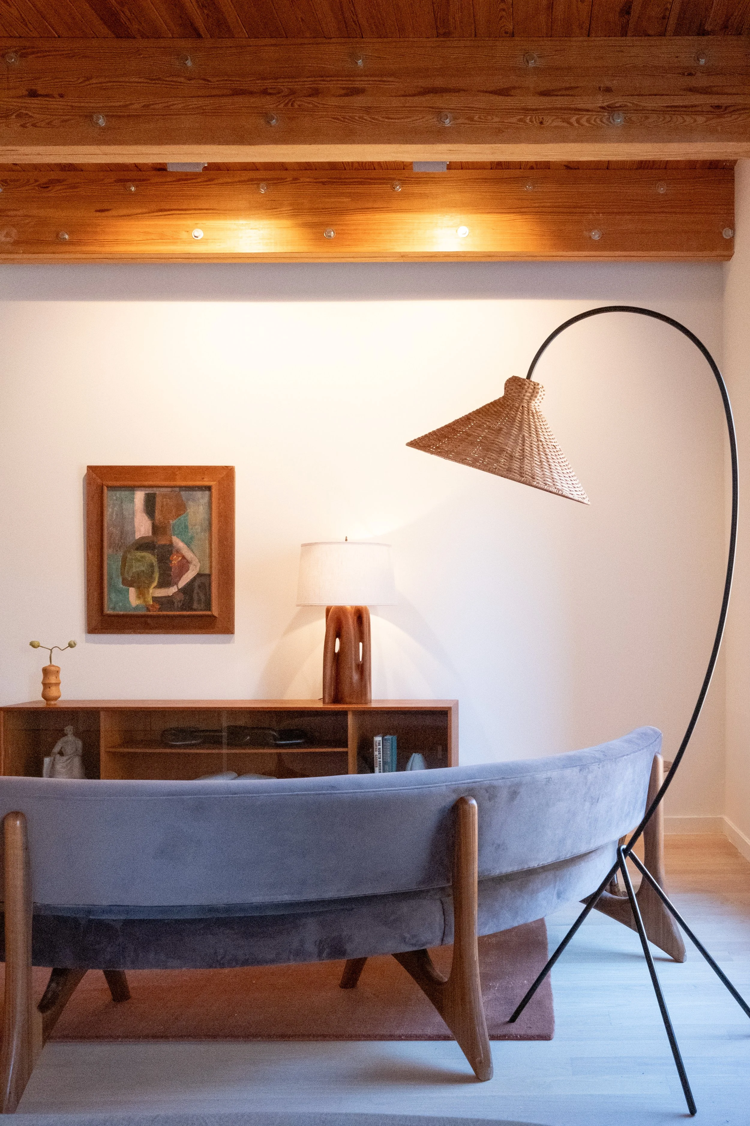 Living room with a gray sofa, wooden cabinet, lamp, framed artwork, and an arc floor lamp with a woven lampshade.