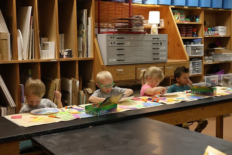 Four children seated at a long table working on art projects