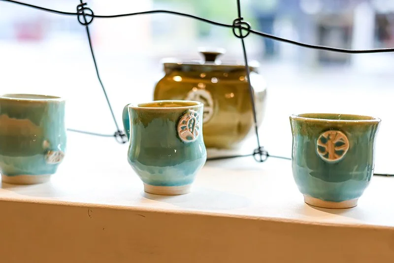 Three ceramic cups with leaf designs beside a large teapot