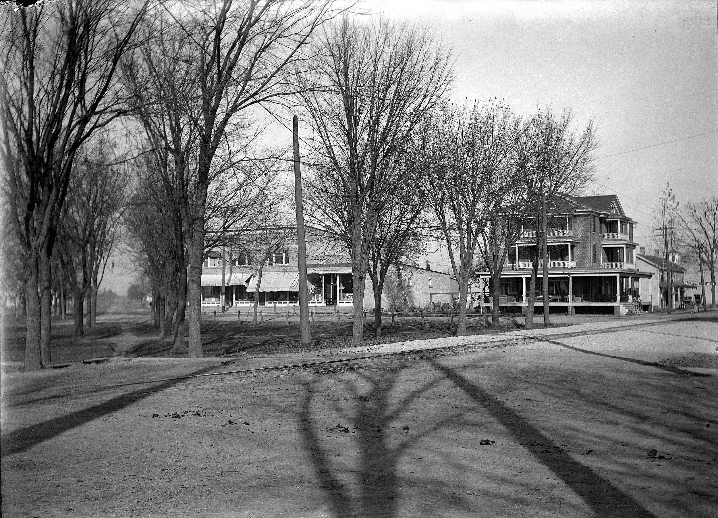 This photograph shows the village square in downtown Walworth, Wisconsin. The buildings are on the north side of the square. The streets are dirt, placing the time of the photo in the early 1900s.
