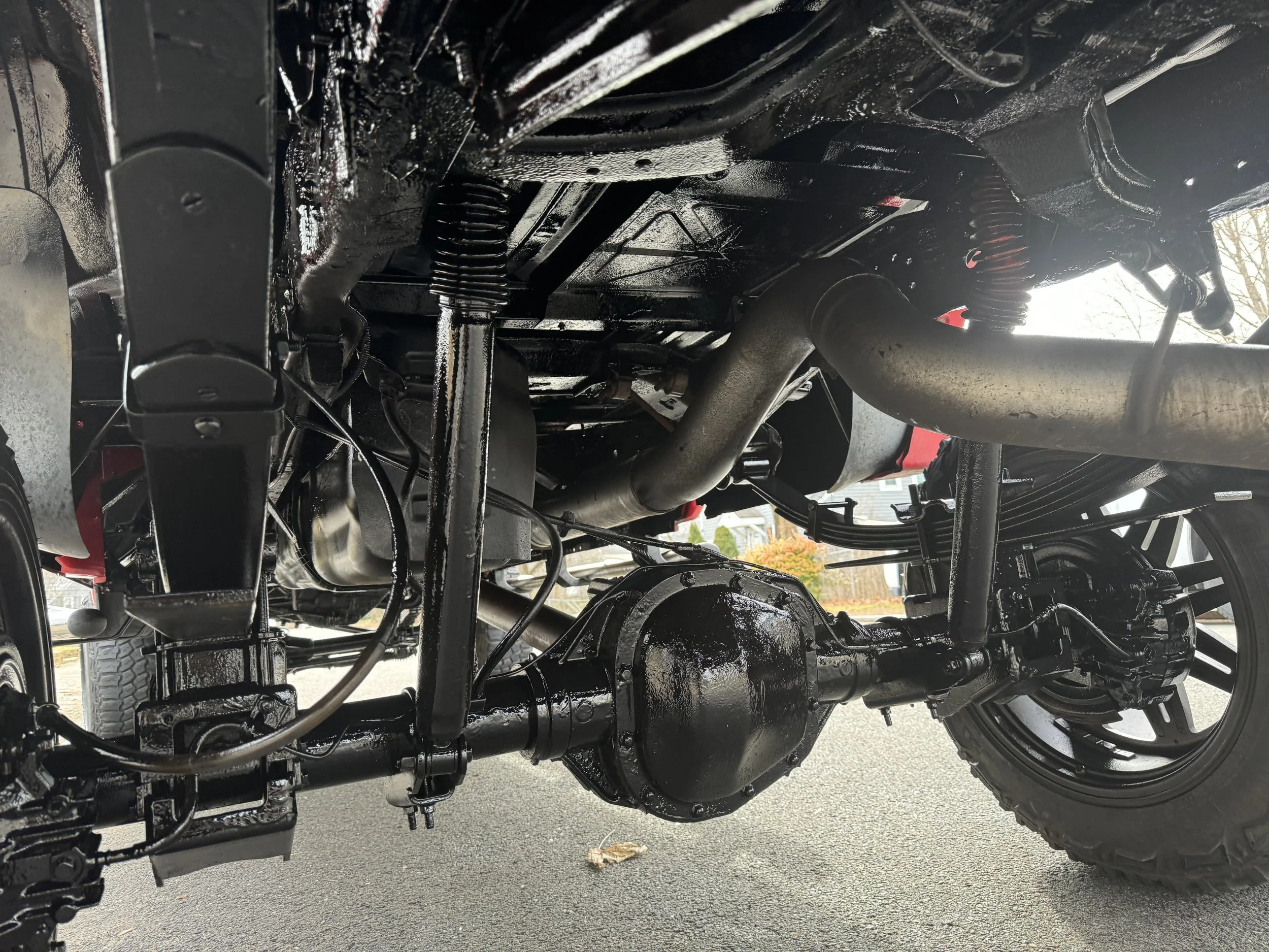 Underside of a vehicle showing suspension, exhaust system, and rear differential on a paved surface
