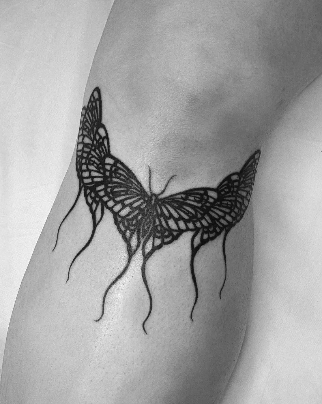 Black butterfly tattoo on person's upper thigh with wings extended and drooping antennae.