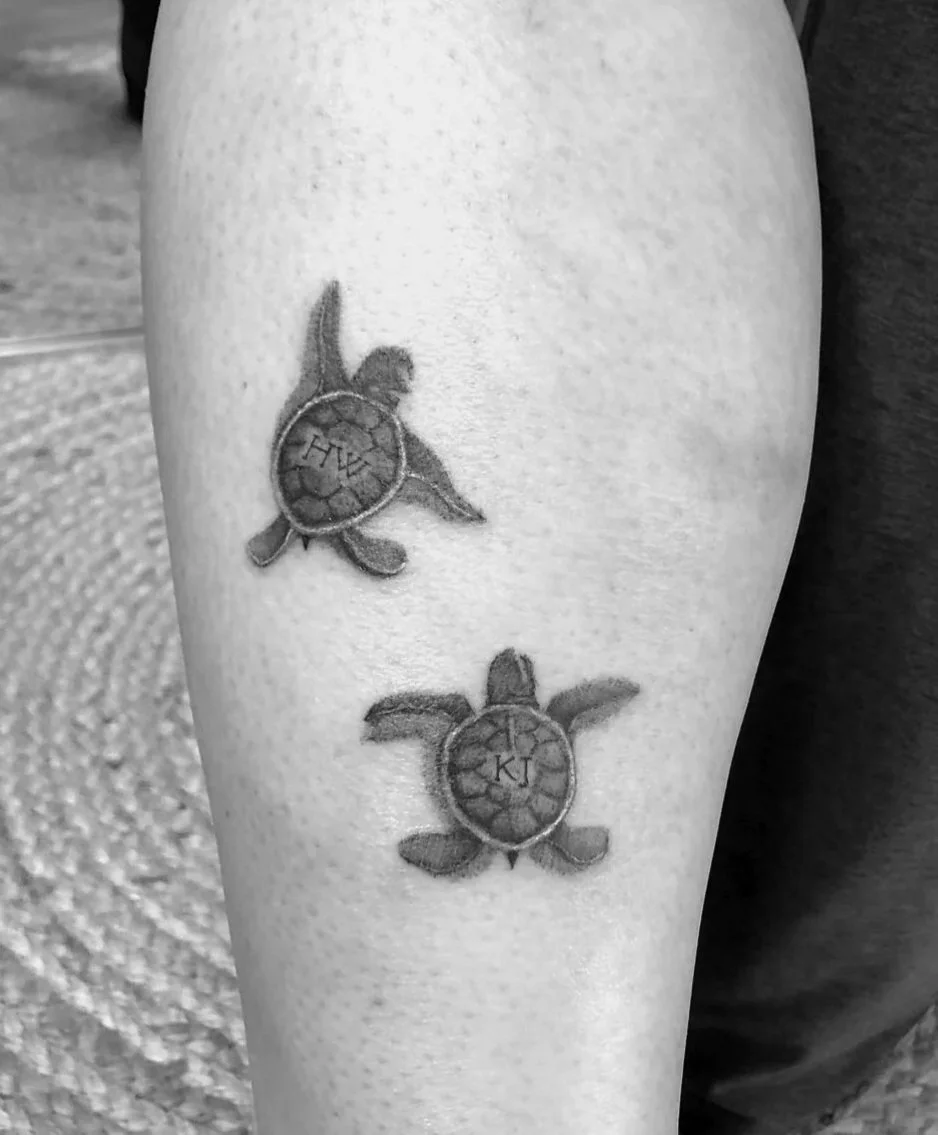 Tattoo of two turtles with initials 'A L' and 'K J' on a person's leg.