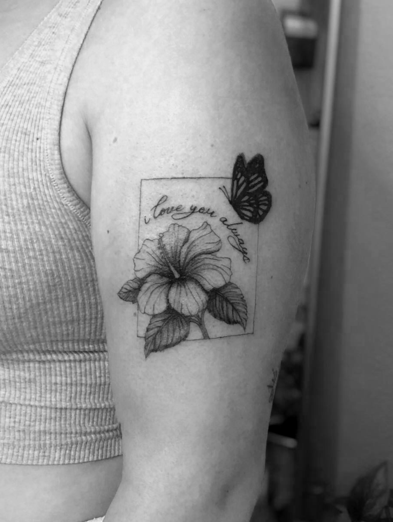 Tattoo of a flower with the words 'I love you, dragon' above it, and a butterfly near the top right corner of the tattoo.