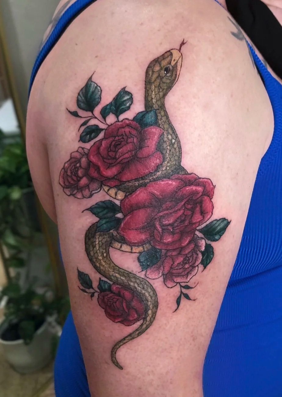 Tattoo of a snake intertwined with red roses on a person's upper arm.
