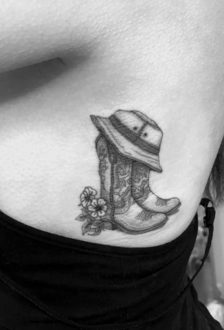 Tattoo of a cowboy boot with a hat and flowers on the person's side