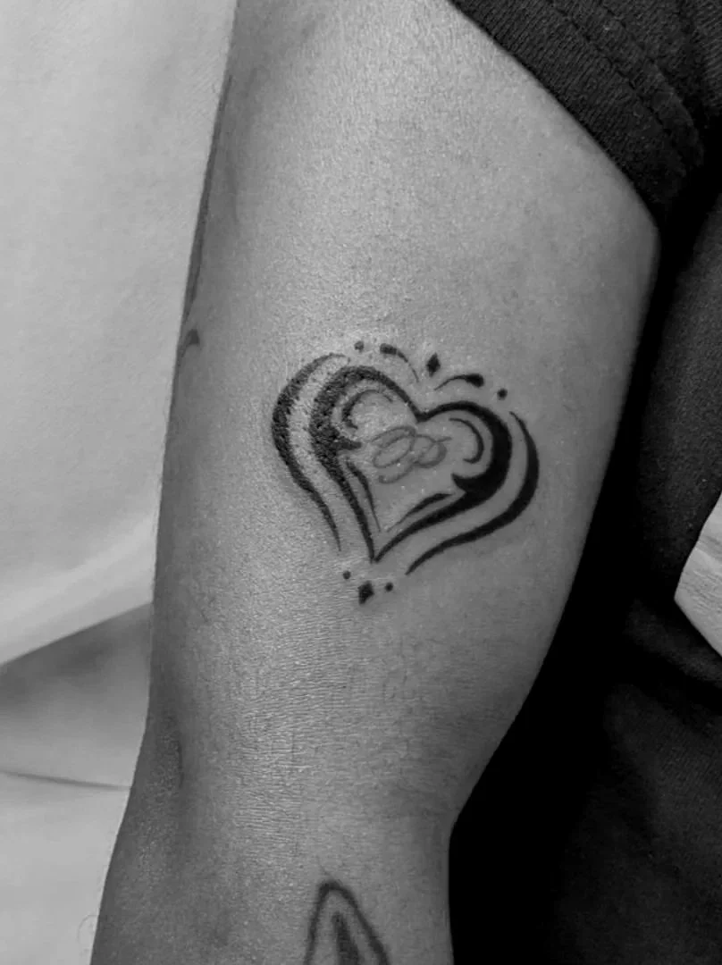 Tattoo of a black and red heart with abstract lines on a person's upper arm.
