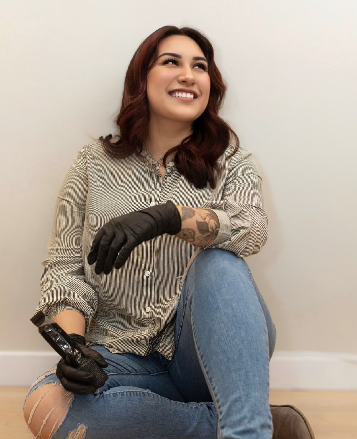A woman with long, wavy, reddish-brown hair smiling at the camera against a plain light gray background.