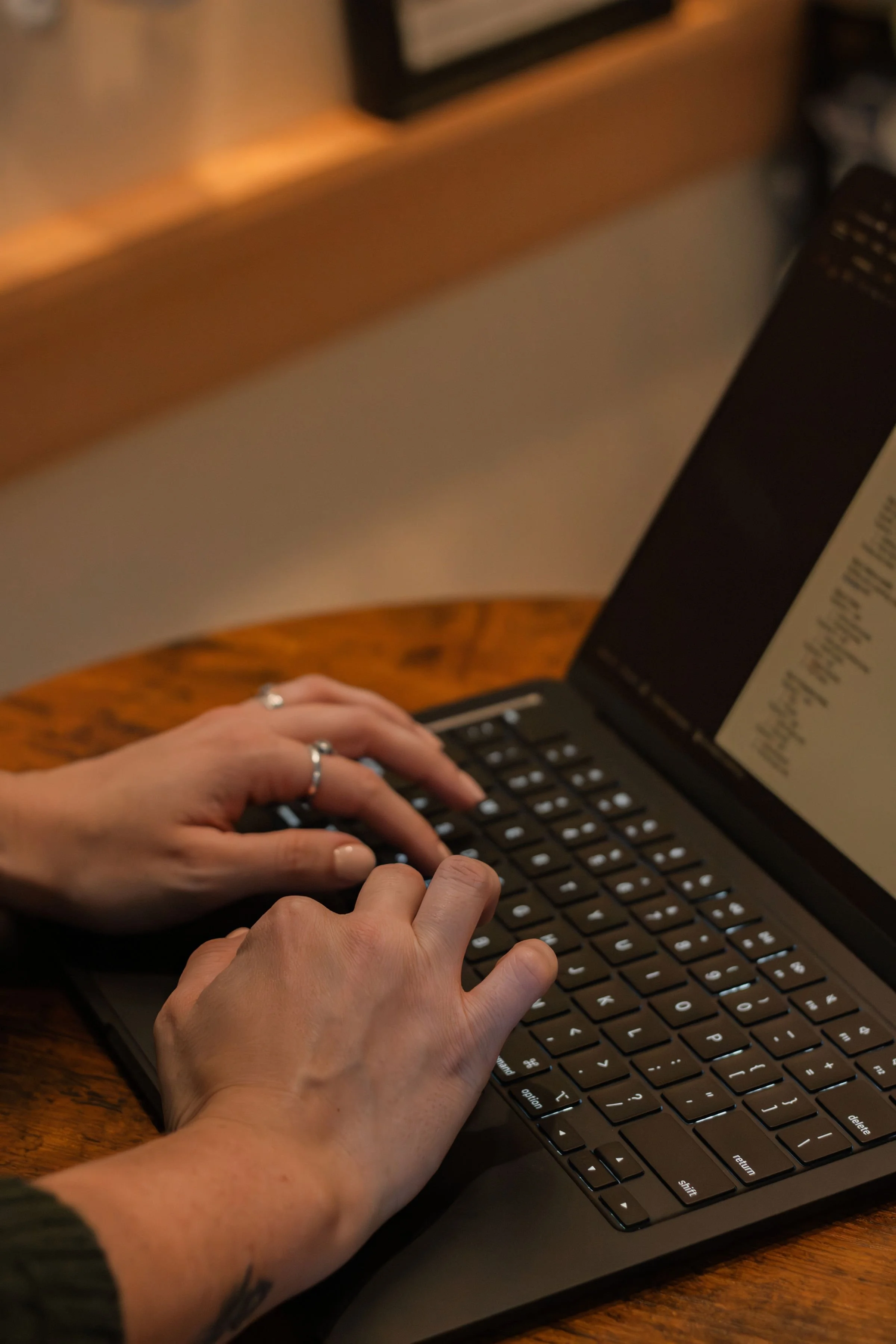 A person typing on a black laptop keyboard, sitting at a wooden table.