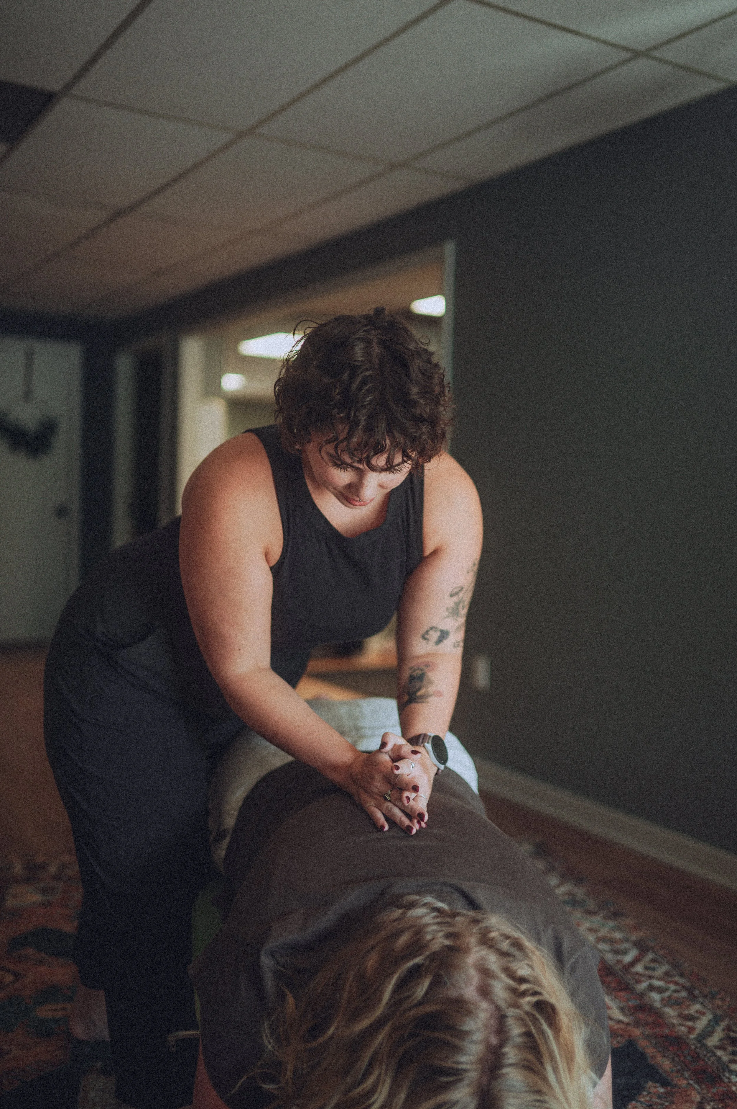 A woman giving an adjustment to a person lying face down on a massage table in a dimly lit room.