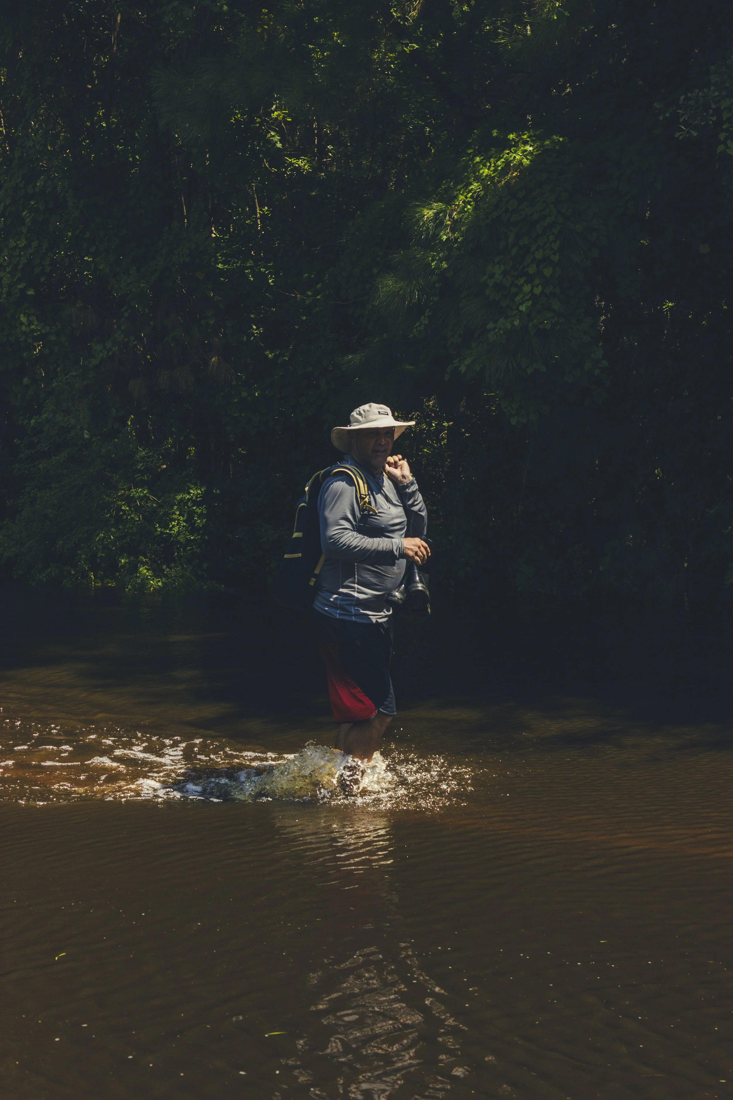 A resident walking through the flooded water carrying boots in his hand