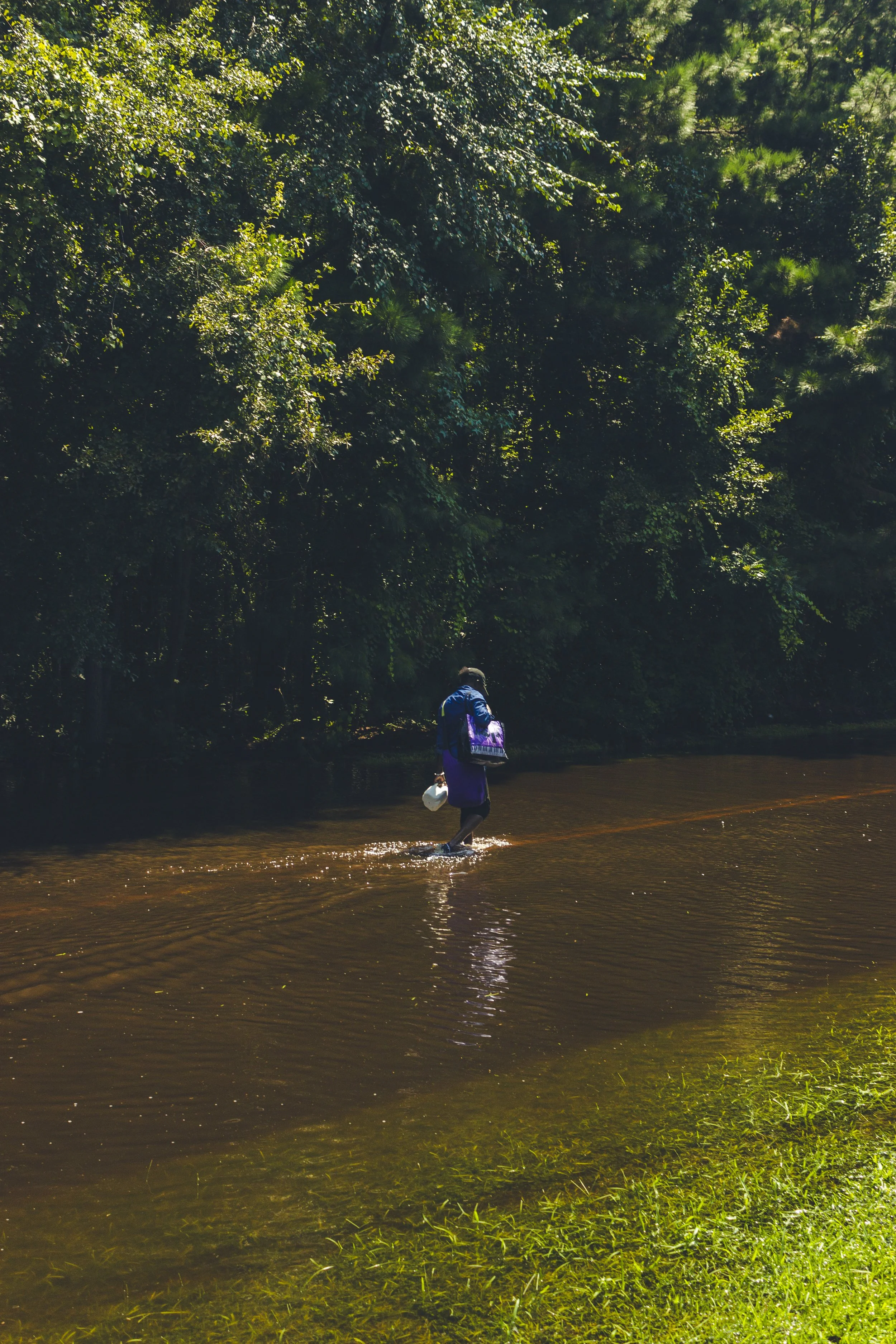A resident walking through the flooded water carrying a bag and a milk jug