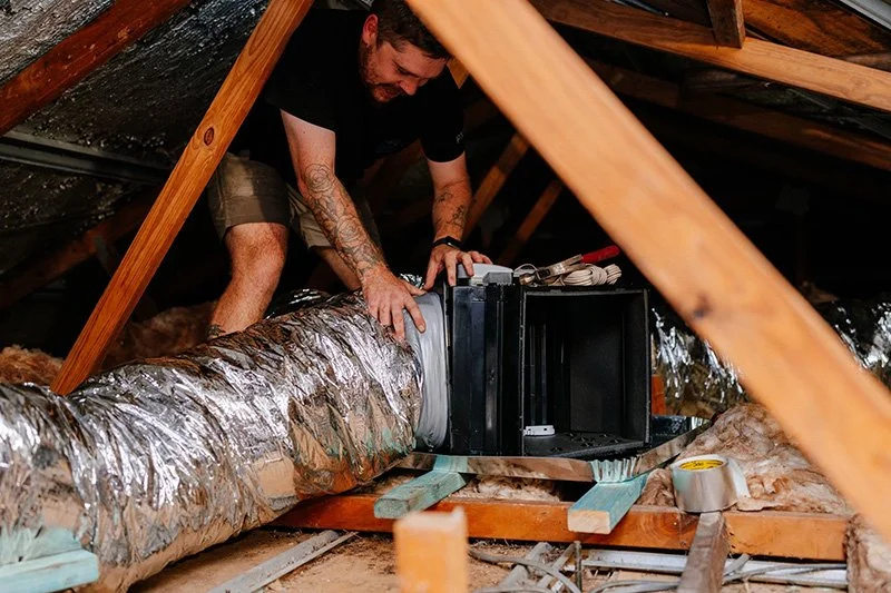 Air conditioning technician installing ducted air conditioning system in roof cavity