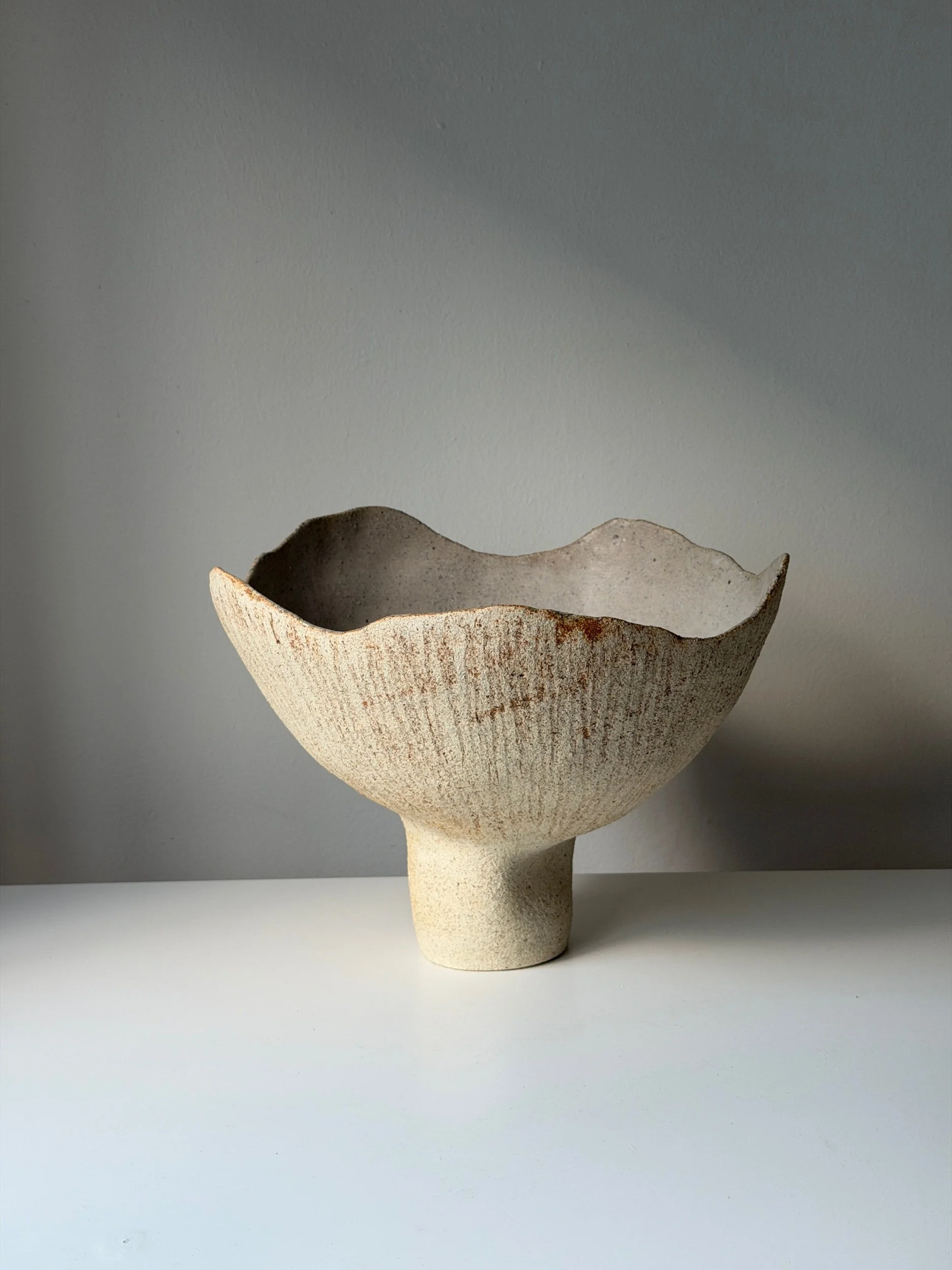 A modern, hand-built ceramic vase in off white textured clay.