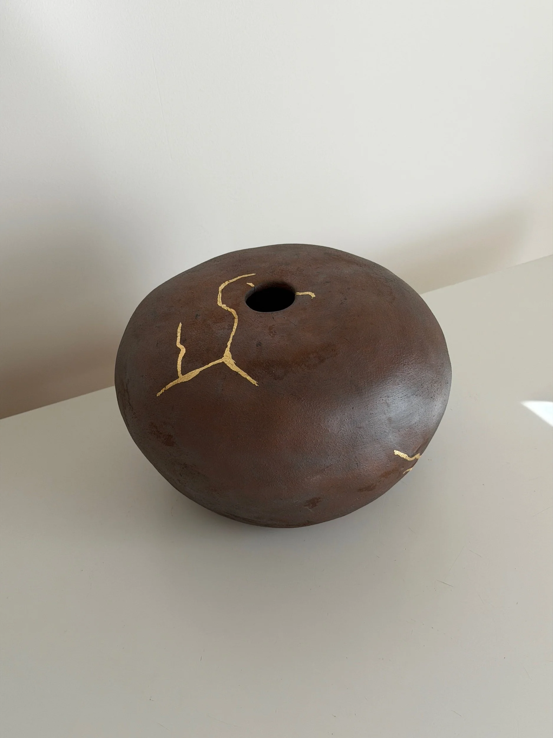 Brown ceramic vase with gold lines, side view on a white surface