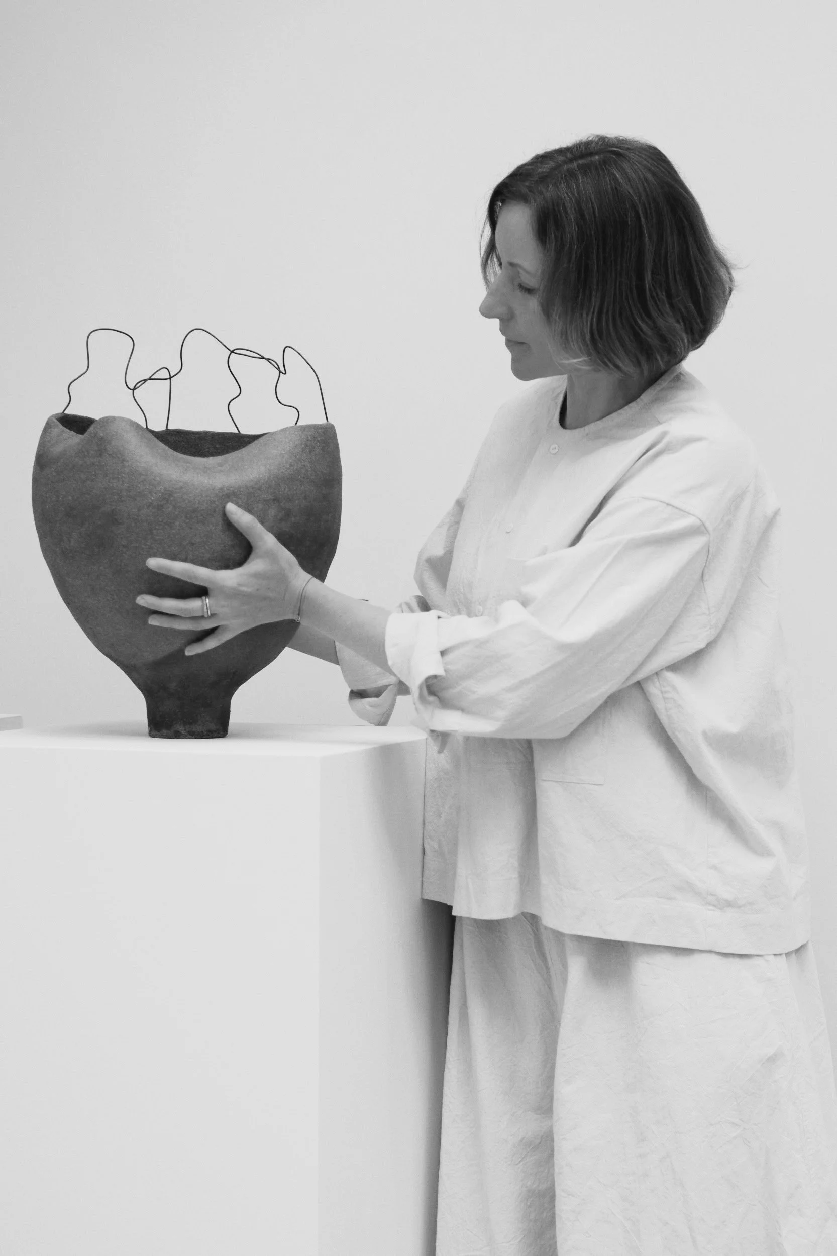 Ceramic artist Anna Shipulina with a hand-built sculptural vessel featuring an organic, petal-like rim in unglazed clay.