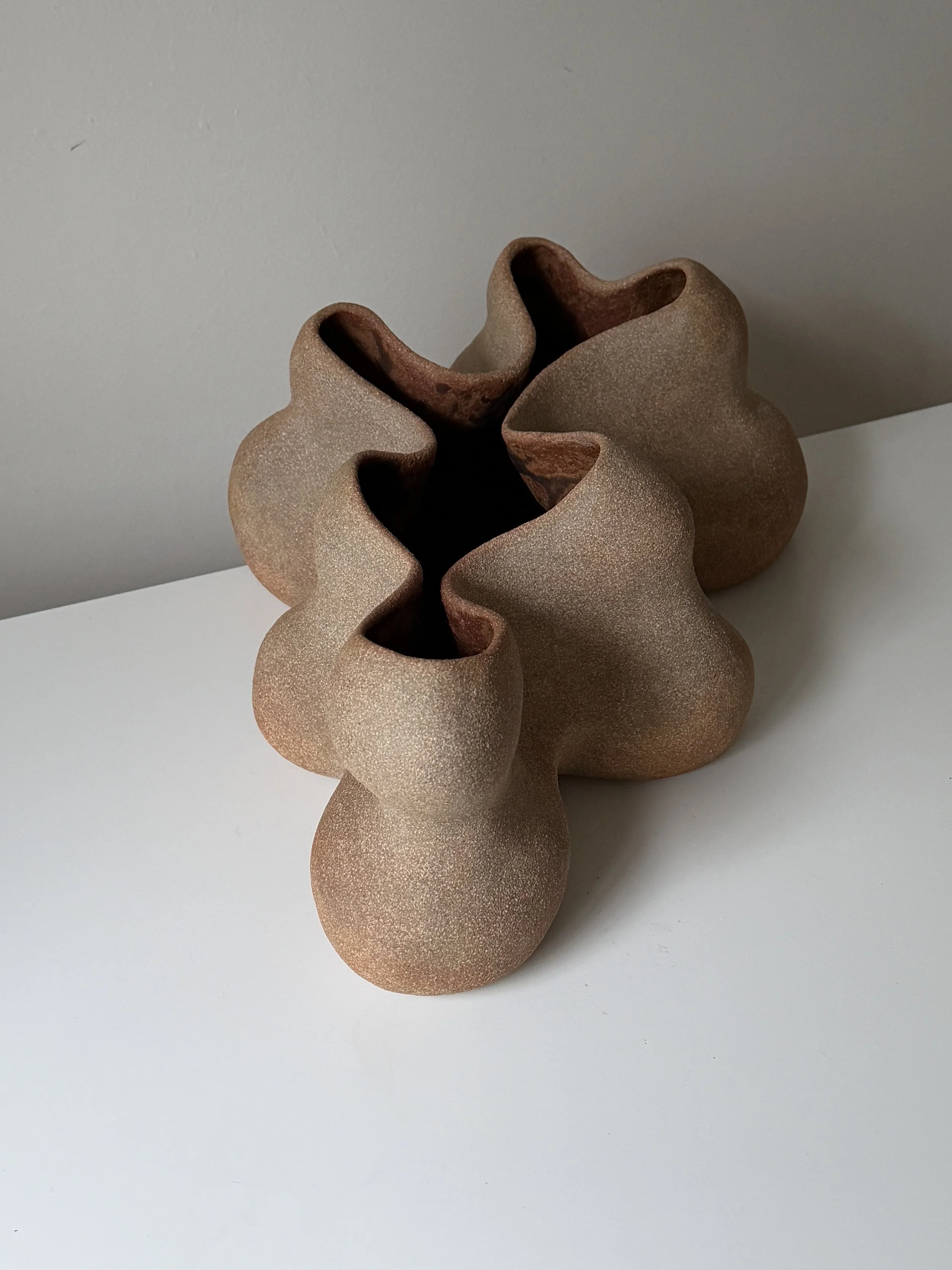Abstract handbuilt ceramic sculpture in warm brown clay with flowing organic contours