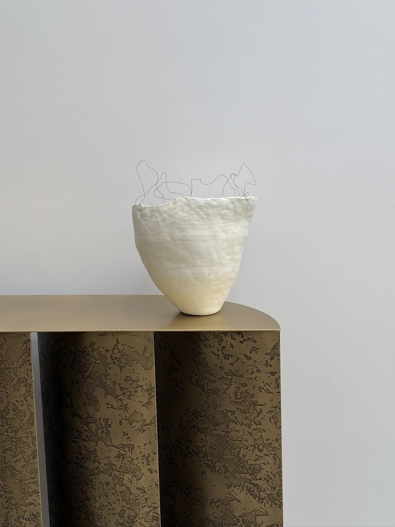 Handbuilt ceramic vase with organic form and delicate wire detail placed on textured pedestal