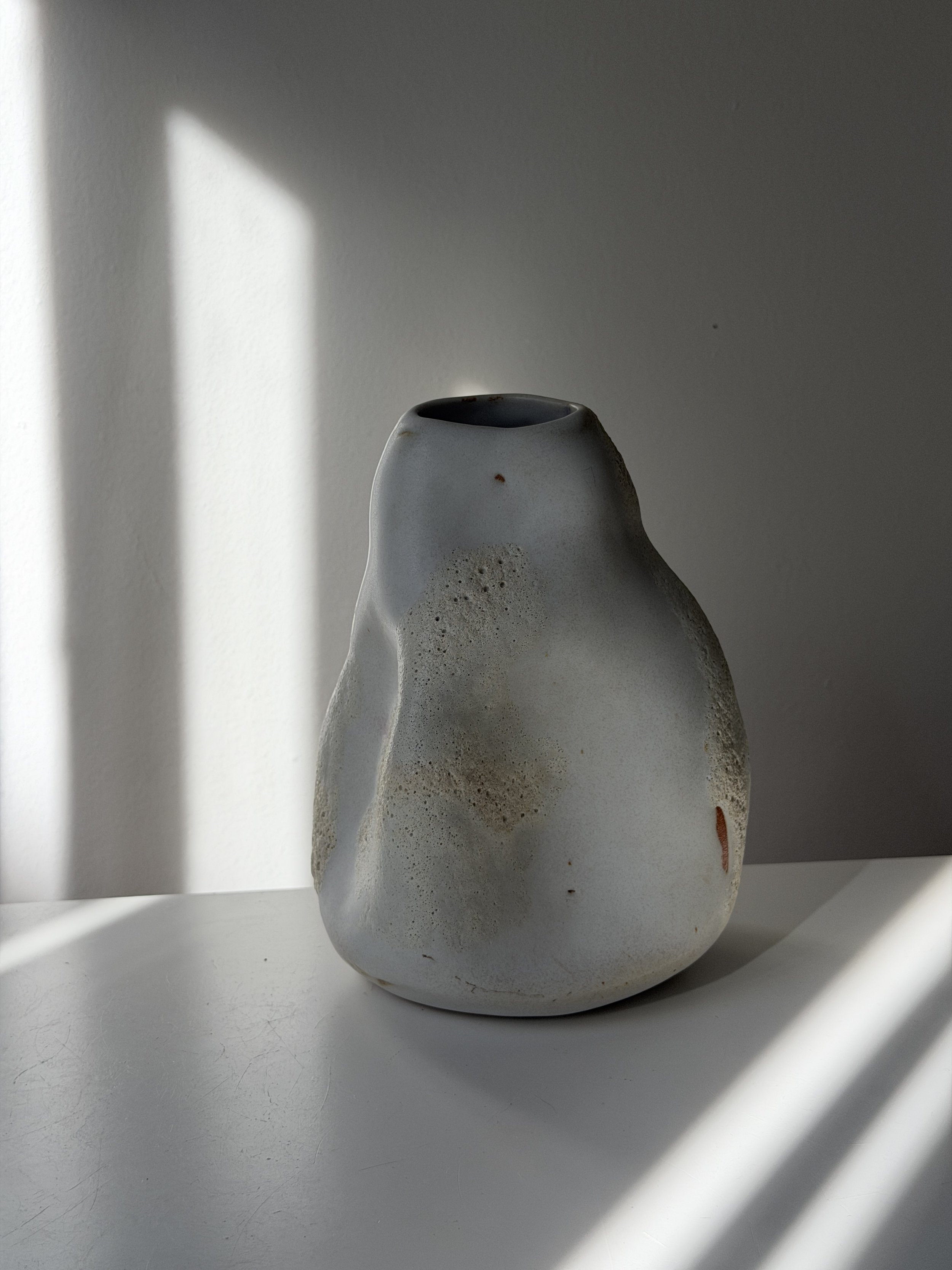 Handmade ceramic vase with matte white glaze and textured lava glaze accents, rounded organic shape, sitting on a neutral background.