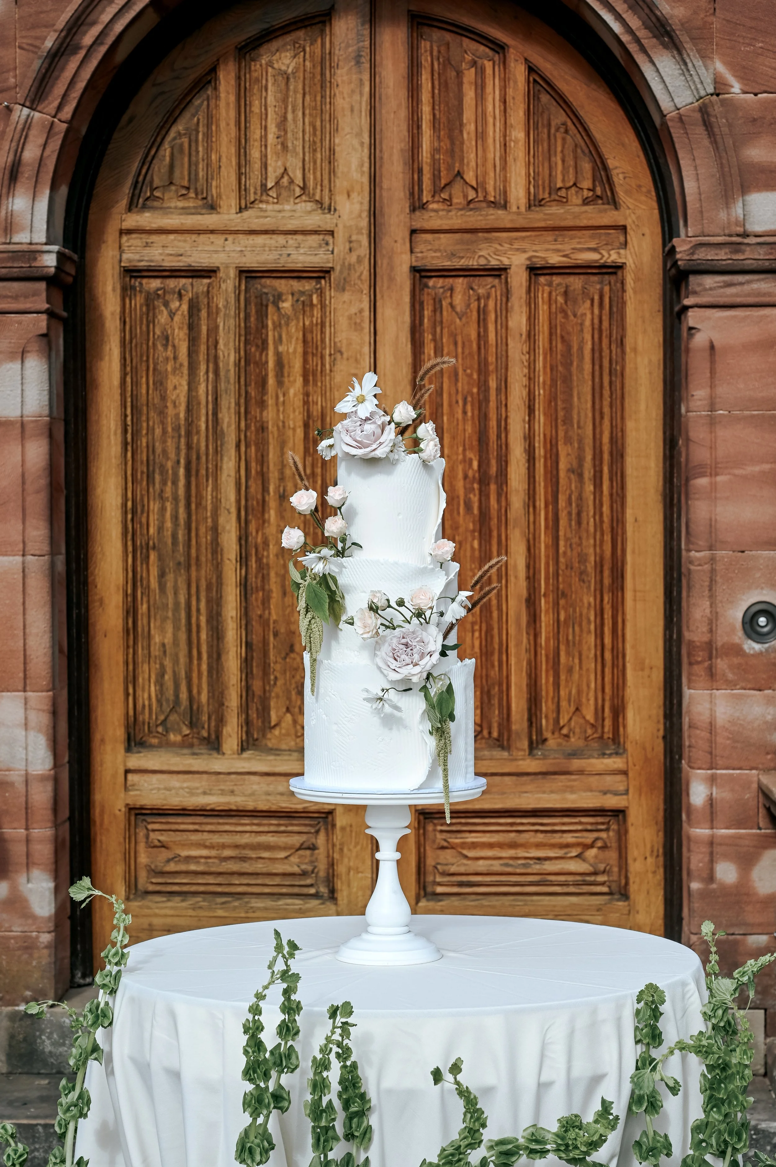 A white wedding cake with flowers outside beautiful venue double doors. 