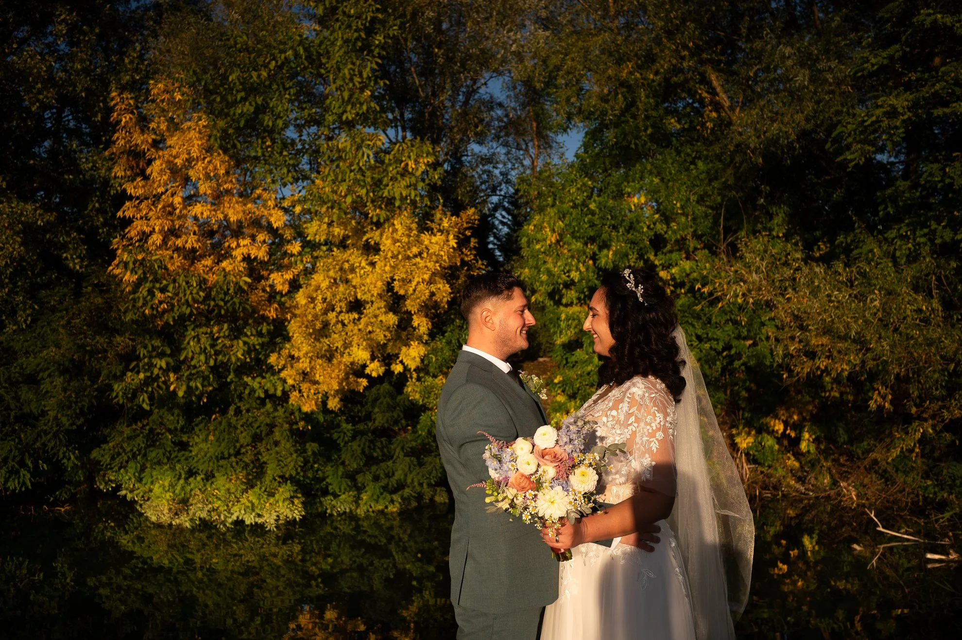 miri privindu-se in dragastos in timpul unei sesiuni foto de toamna imbracati in mire si mireasa pe malul unui lac