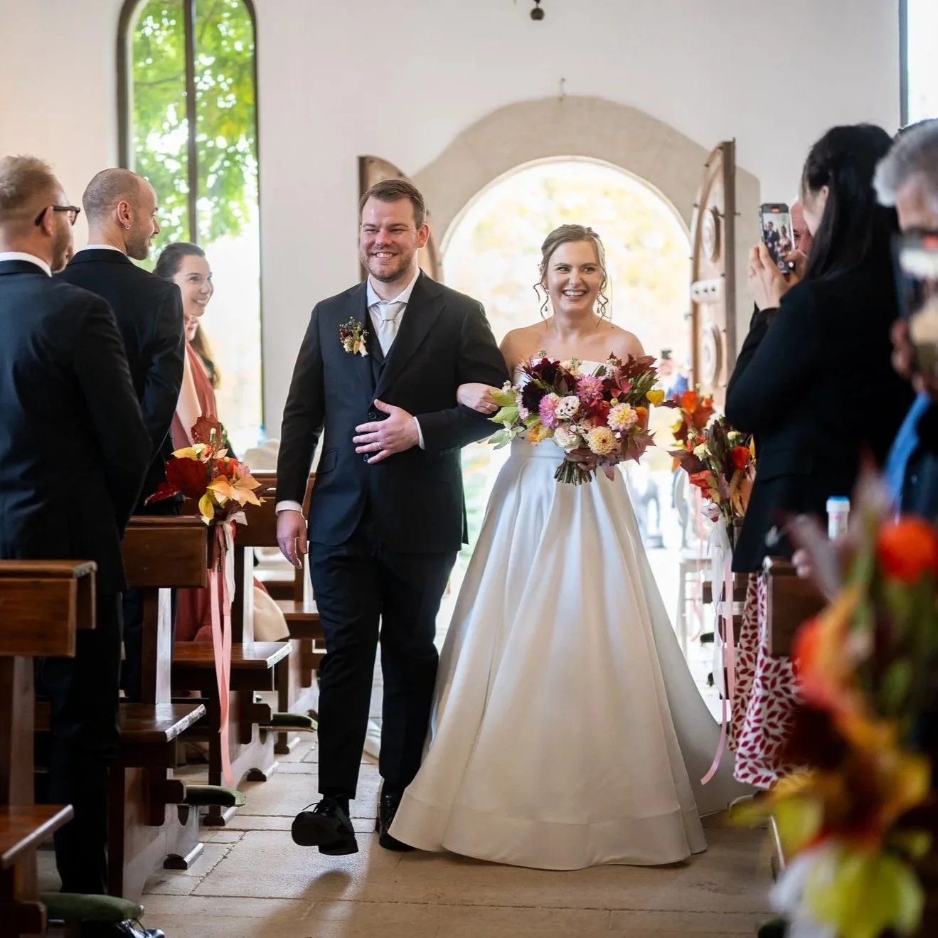 mire si mireasa intrand in biserica catolica printre strane unde invitatii stau in picioare si aplauda