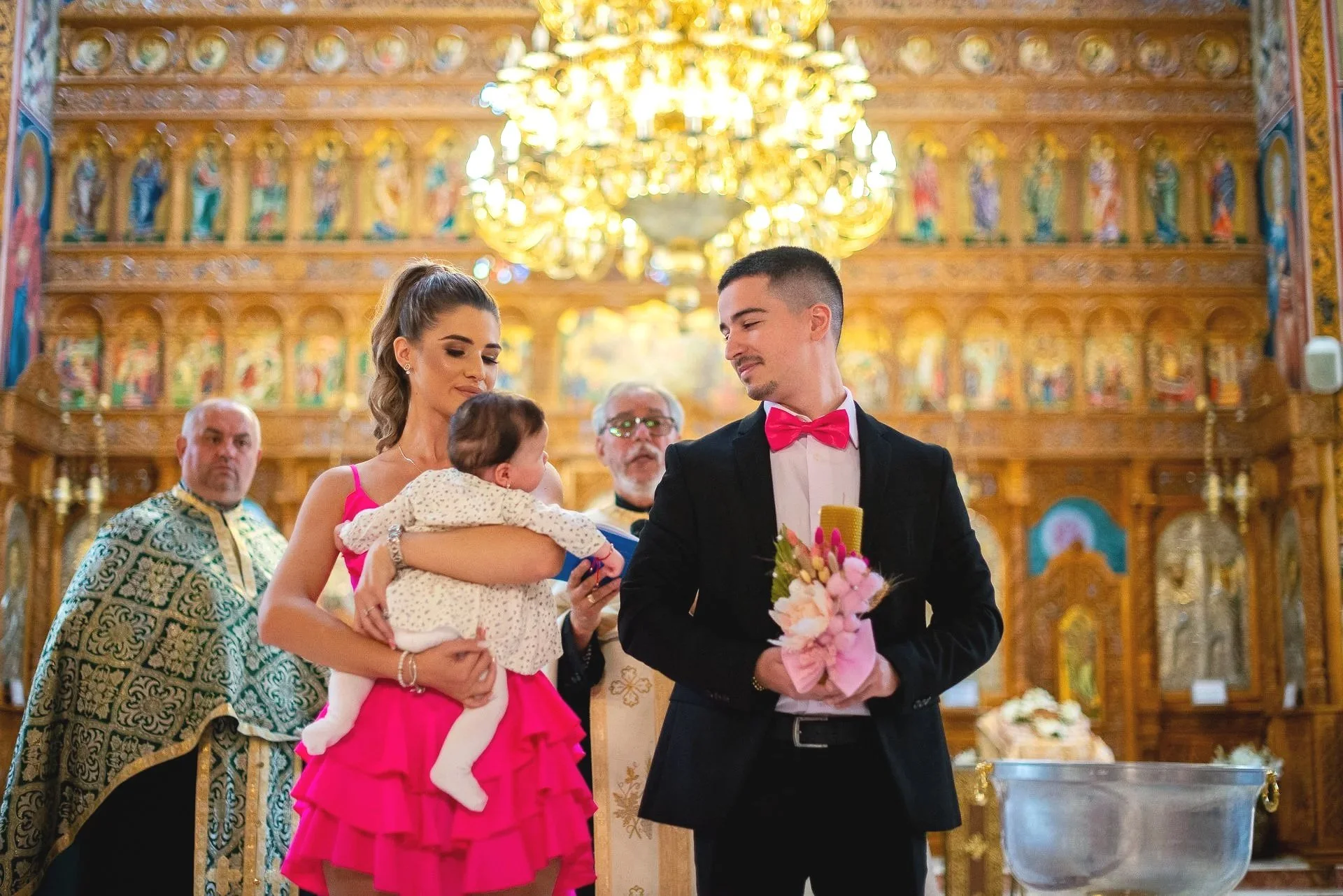 Fotografie de botez cu Vanessa Maria în biserică, alături de părinți și nași, surprinsă în timpul ceremoniei religioase