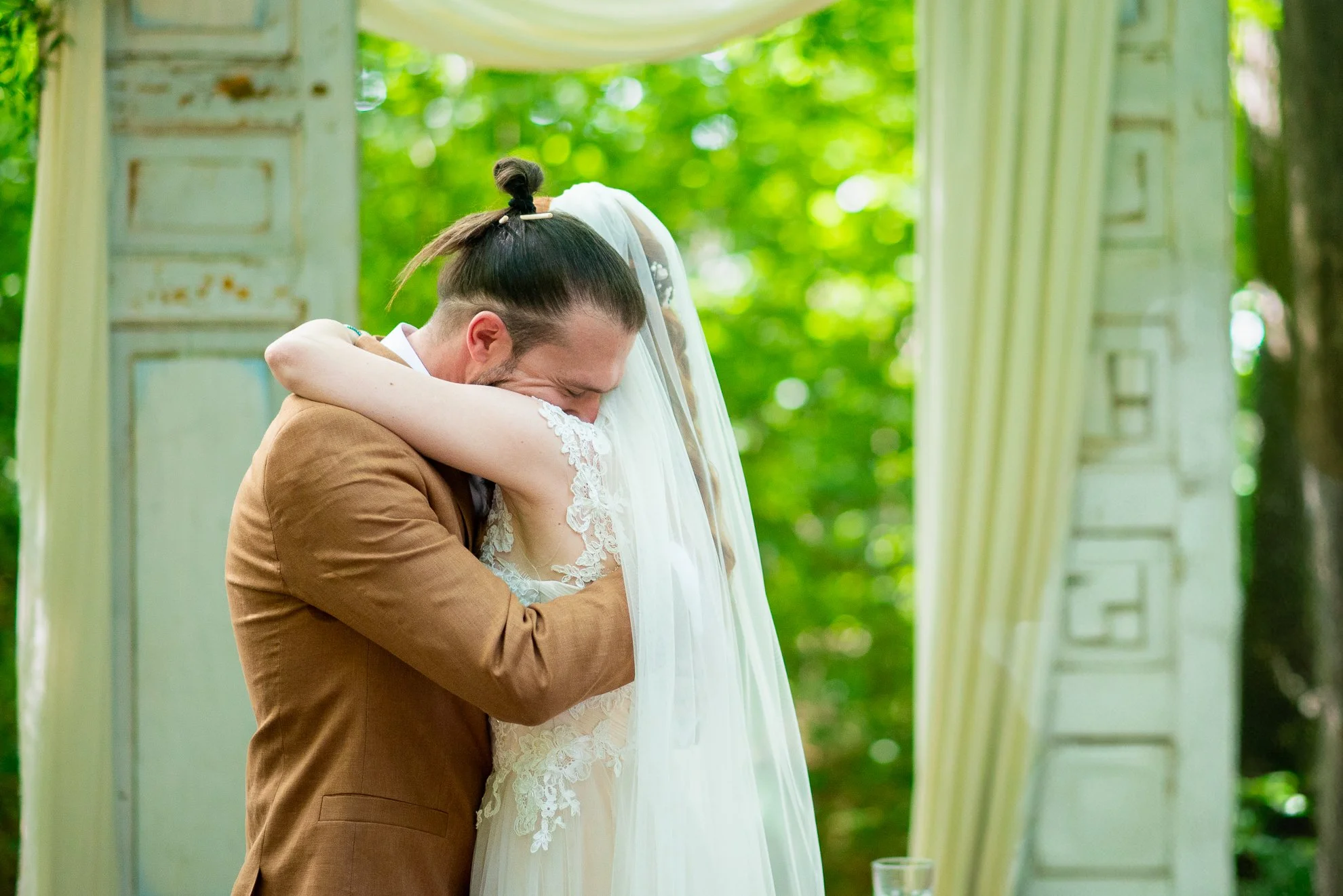 Îmbrățișare emoționantă între miri în timpul ceremoniei de nuntă, într-un cadru natural